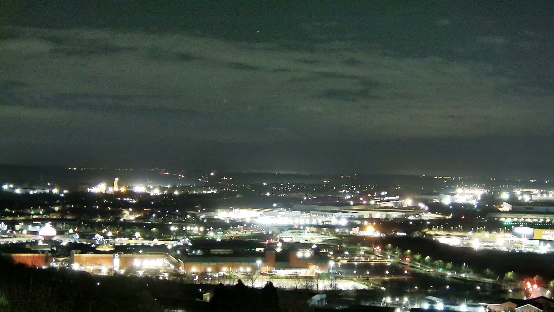 A nighttime view of a city illuminated by lights under a cloudy sky.