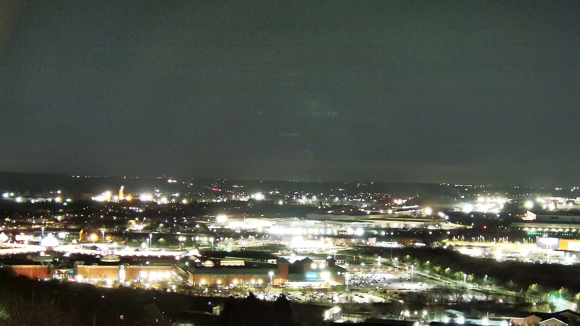 A nighttime, high-angle view of a sprawling city illuminated by numerous lights, under a dark sky.