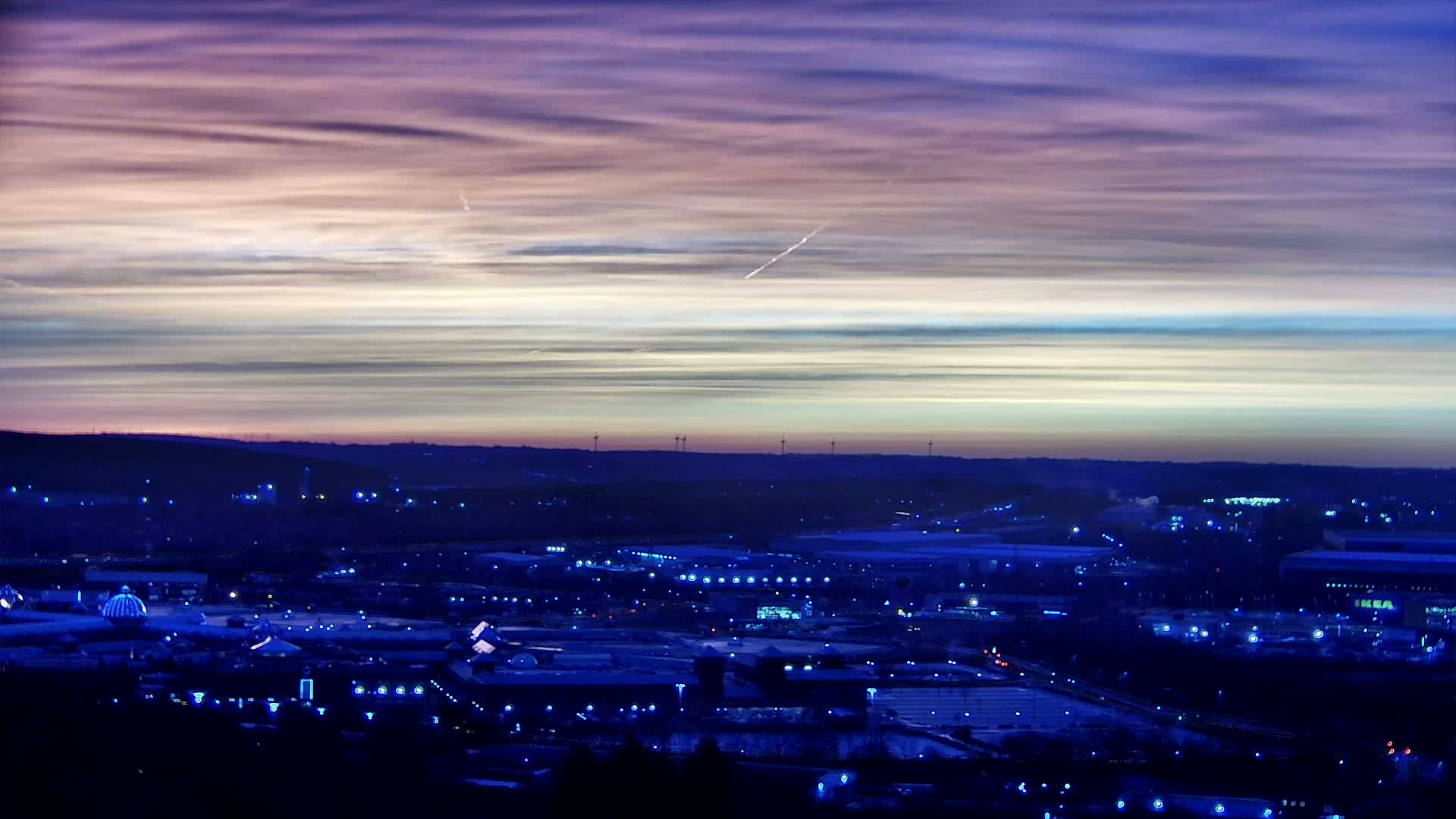 A sprawling cityscape at twilight, illuminated by scattered lights below a soft, multi-hued sky.