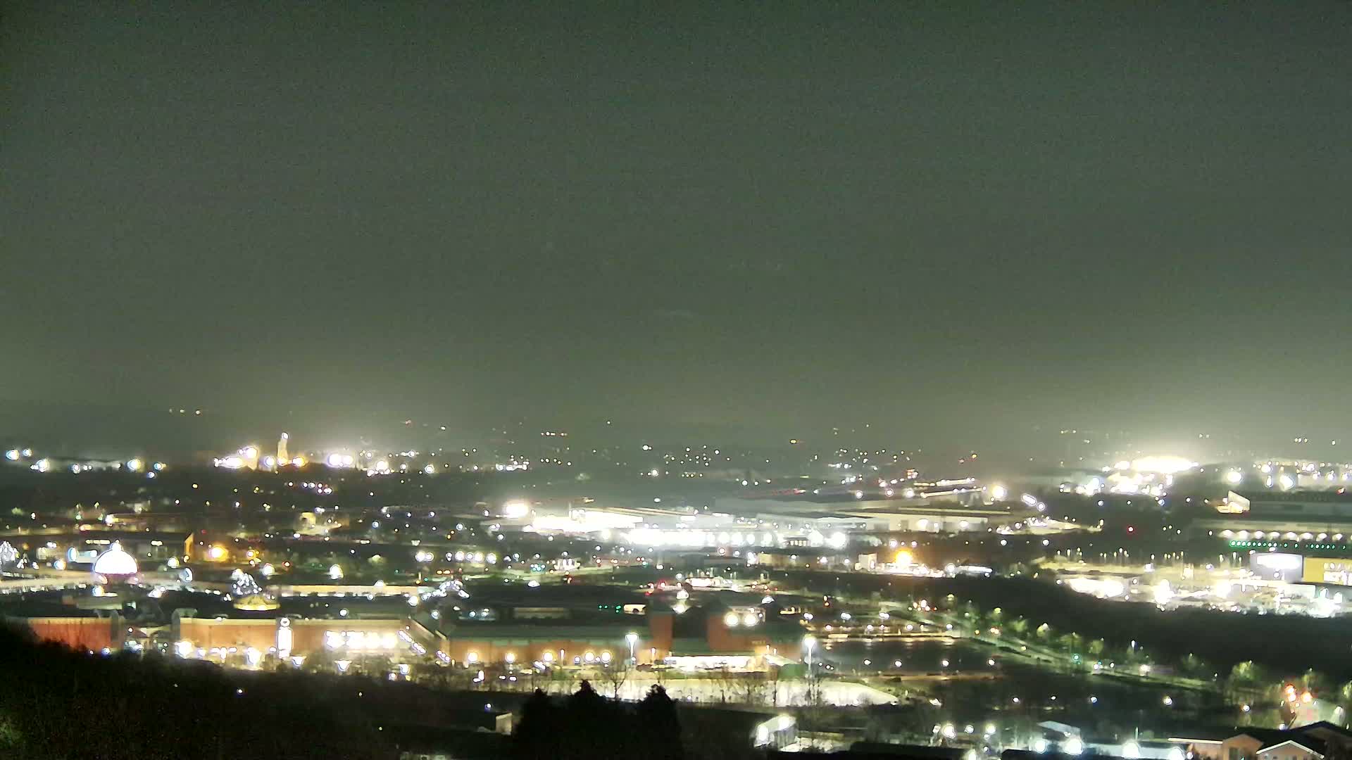 A nighttime view of a sprawling city illuminated by numerous lights under a hazy, dark sky.