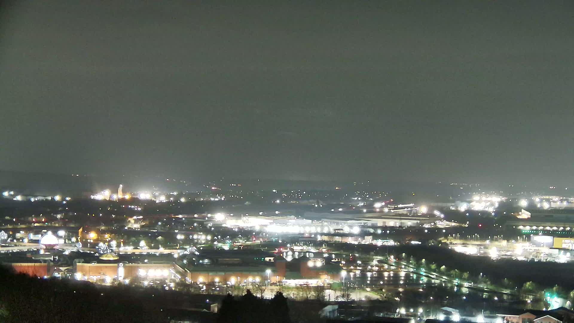 A nighttime view of a sprawling city illuminated by numerous lights under a dark, overcast sky.