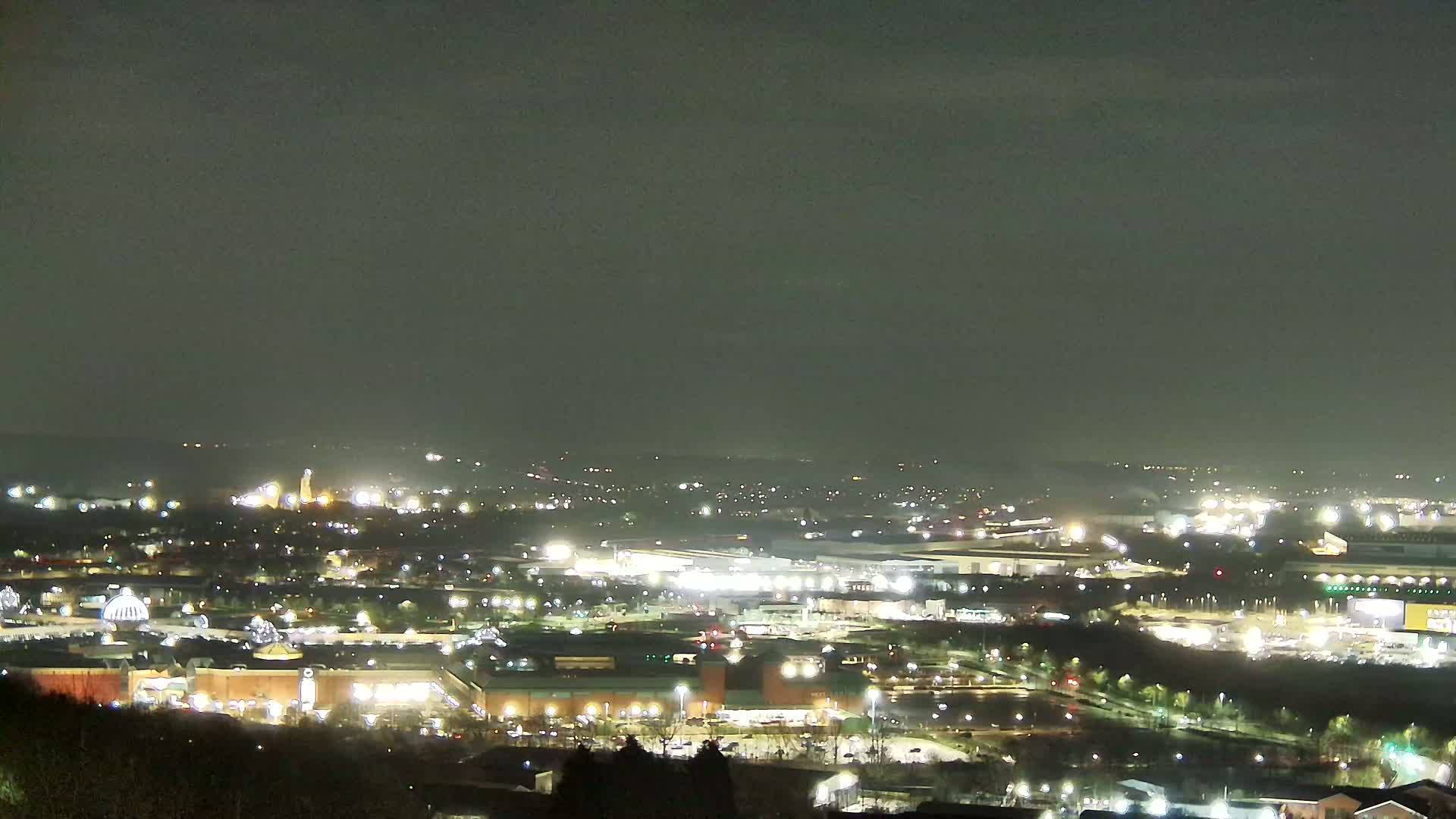 A nighttime, high-angle view of a sprawling city illuminated by numerous lights, under a dark, overcast sky.