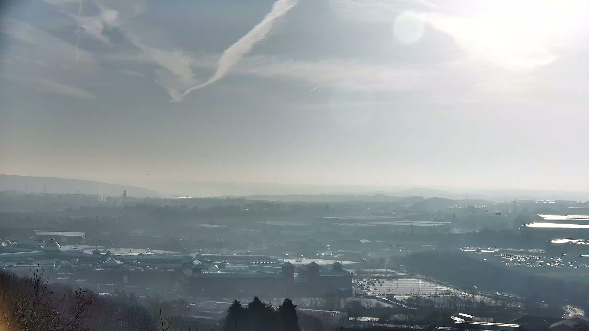A hazy, sunny day reveals a sprawling cityscape and large parking lots viewed from a distant elevated perspective.