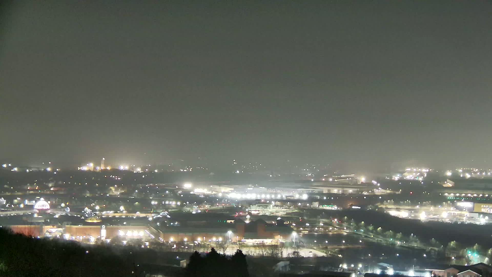 A nighttime, hazy view of a sprawling city landscape, featuring numerous illuminated buildings and roads.