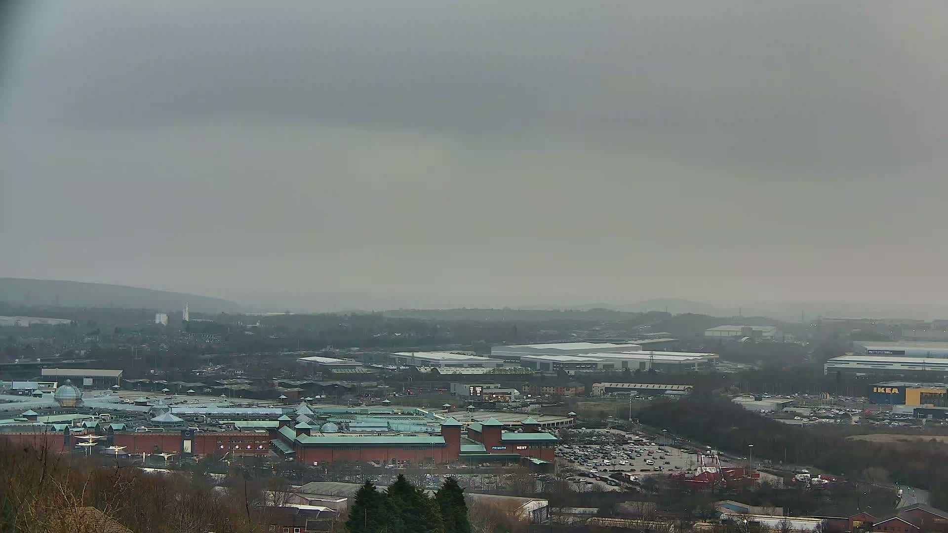 A large shopping mall and surrounding industrial buildings are visible under a hazy, overcast sky.