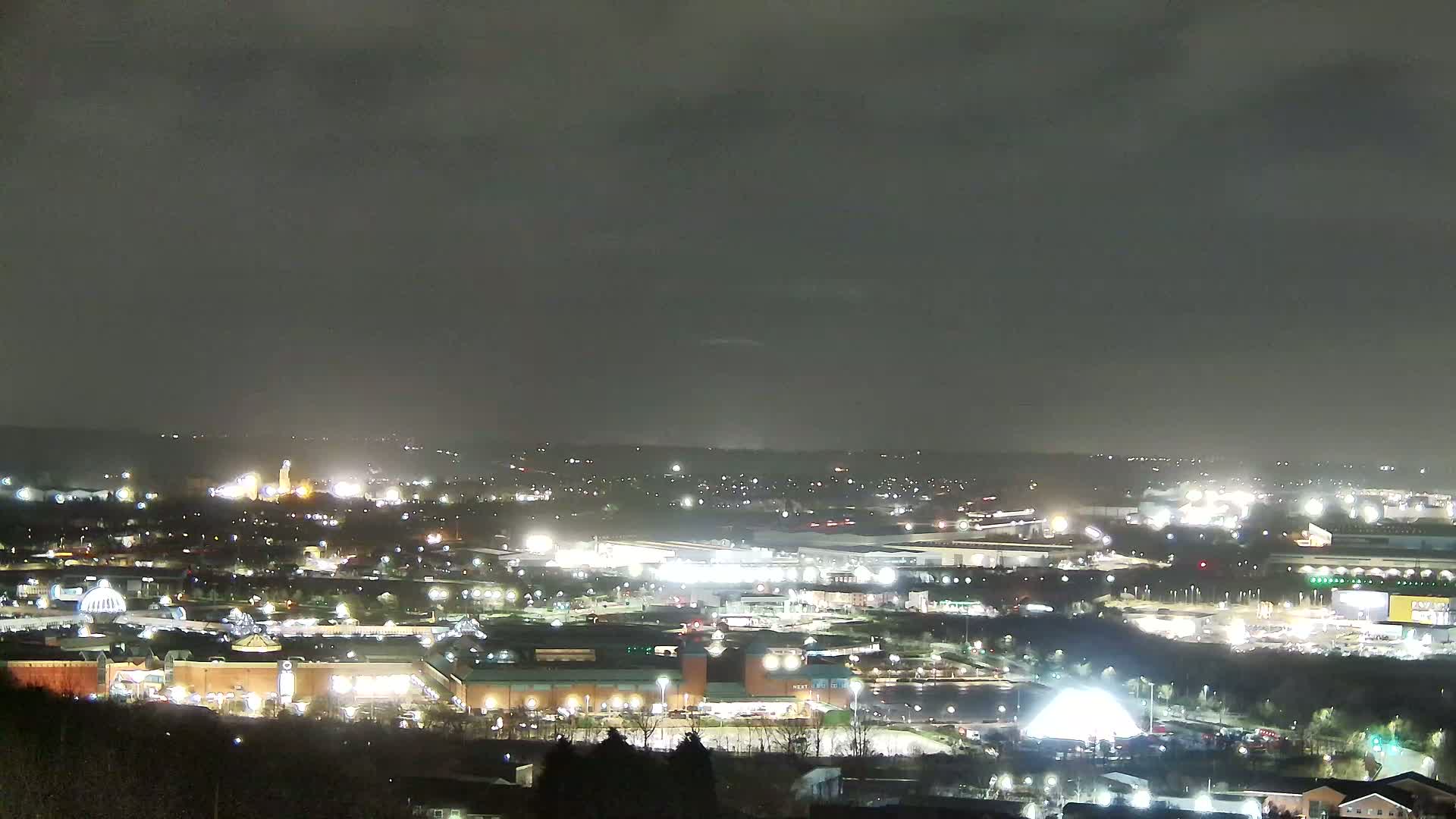 A nighttime, overcast view of a sprawling city landscape, illuminated by numerous lights from buildings and businesses.