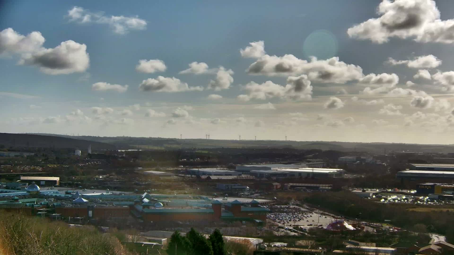 A high-angle view of a sprawling shopping center and industrial park under a partly cloudy, sunny sky.