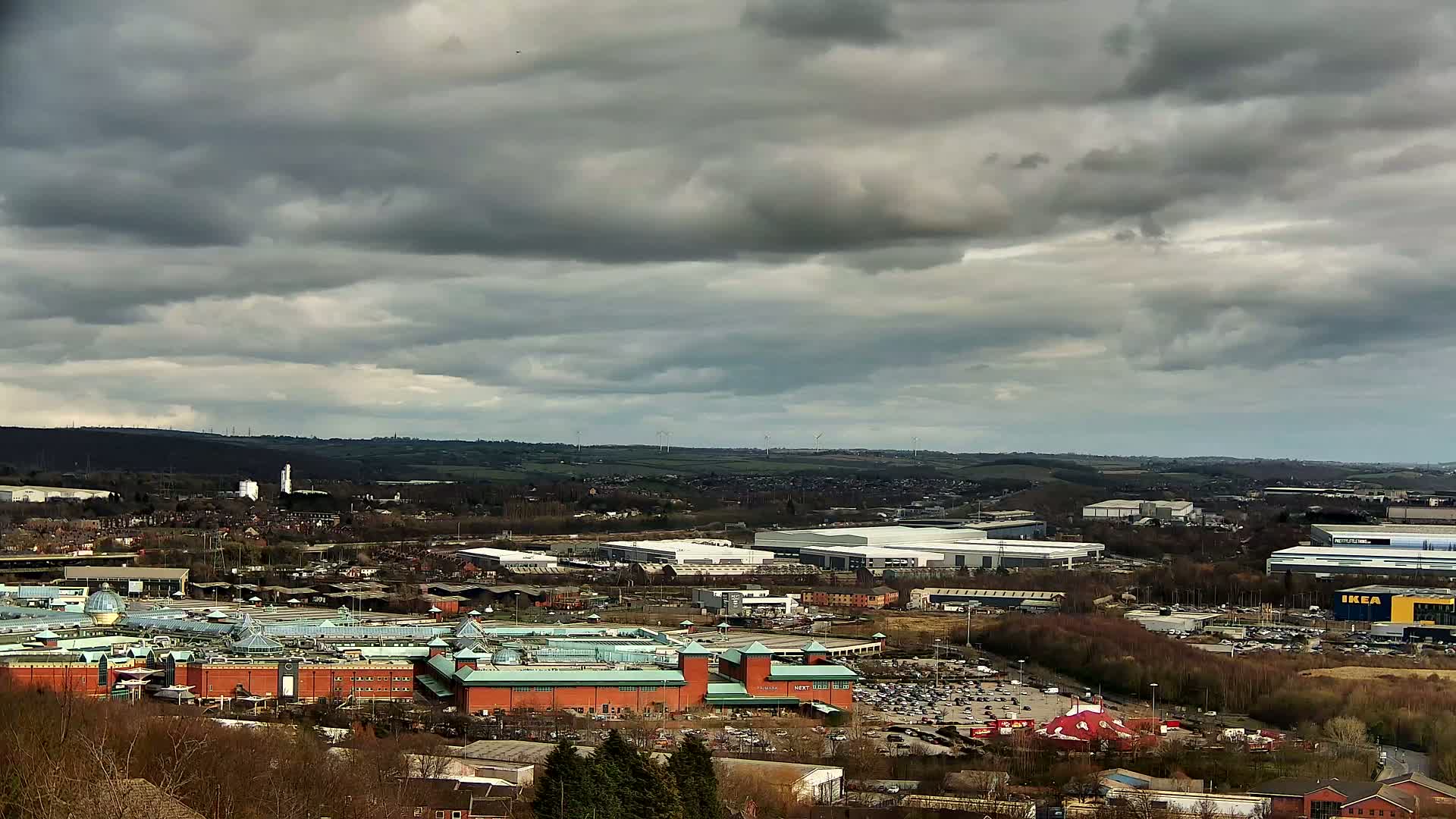 A large shopping mall and surrounding industrial areas are visible under a cloudy sky.