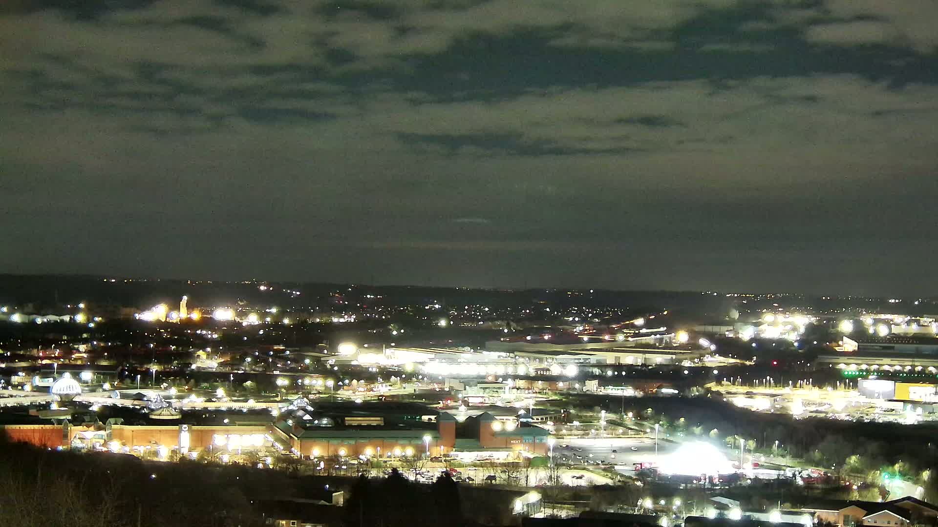 A sprawling, illuminated cityscape at night under a mostly cloudy sky.