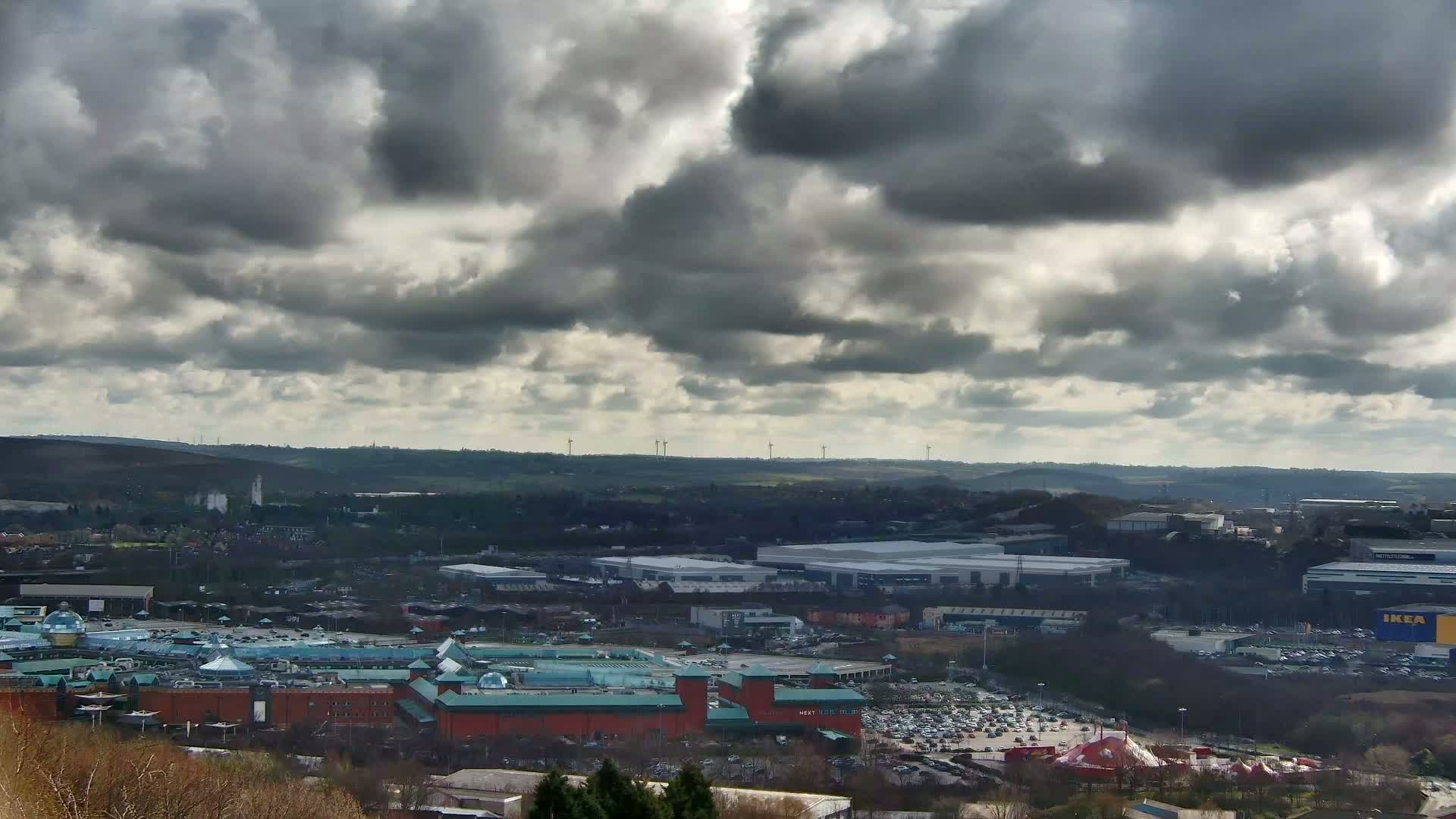 A large shopping center and surrounding industrial park are visible beneath a mostly cloudy sky.