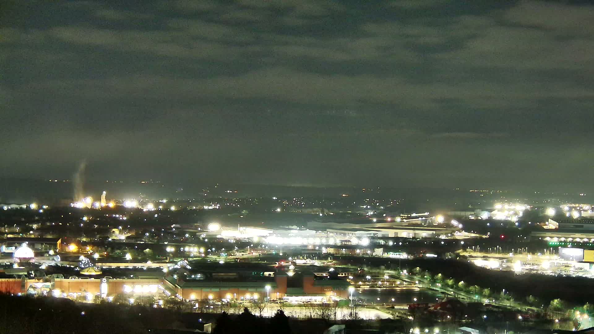 A nighttime, high-angle view of a city illuminated by artificial lights under a cloudy sky.