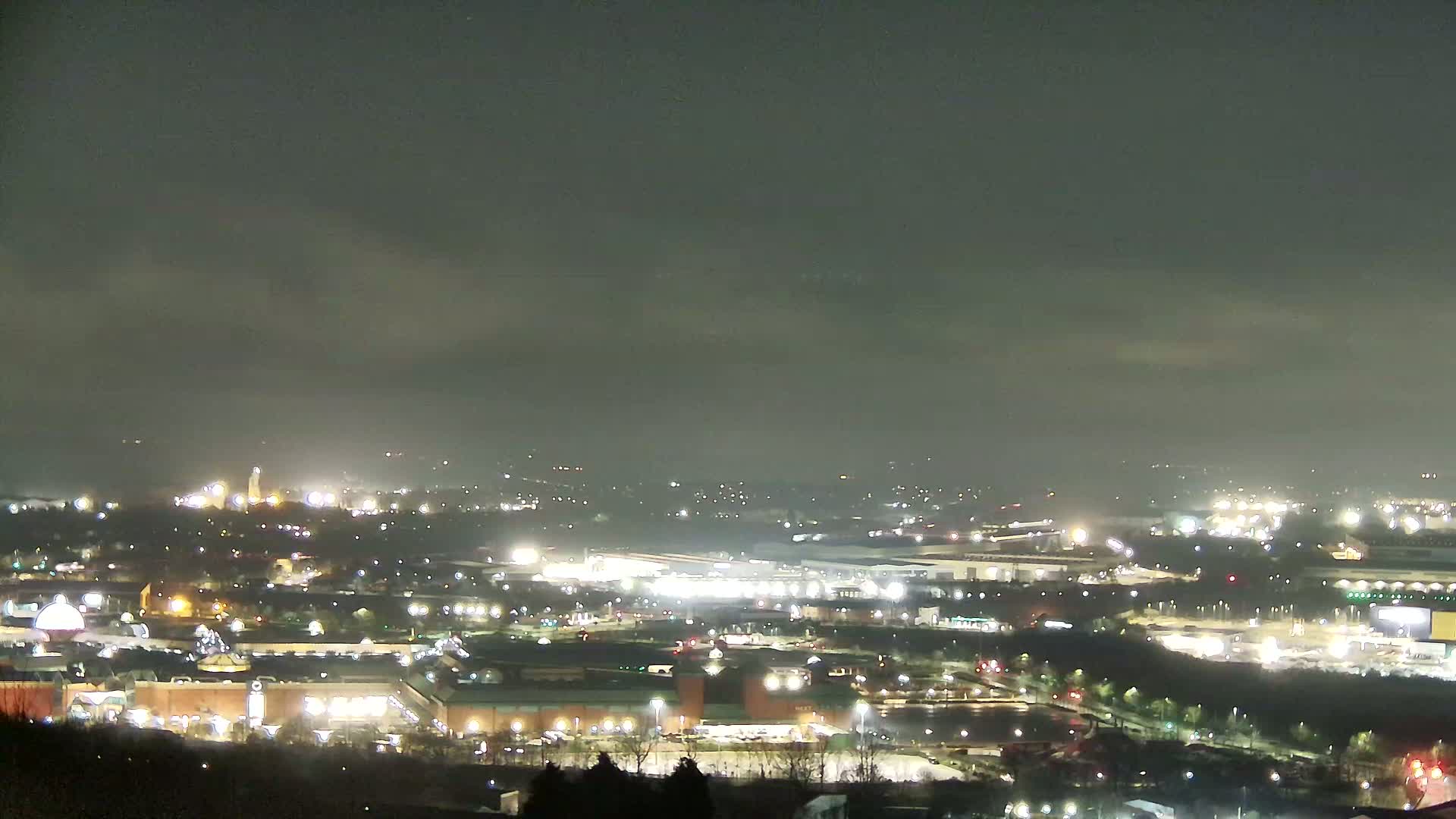 A nighttime, hazy view of a sprawling city illuminated by numerous lights, seen from a high vantage point.