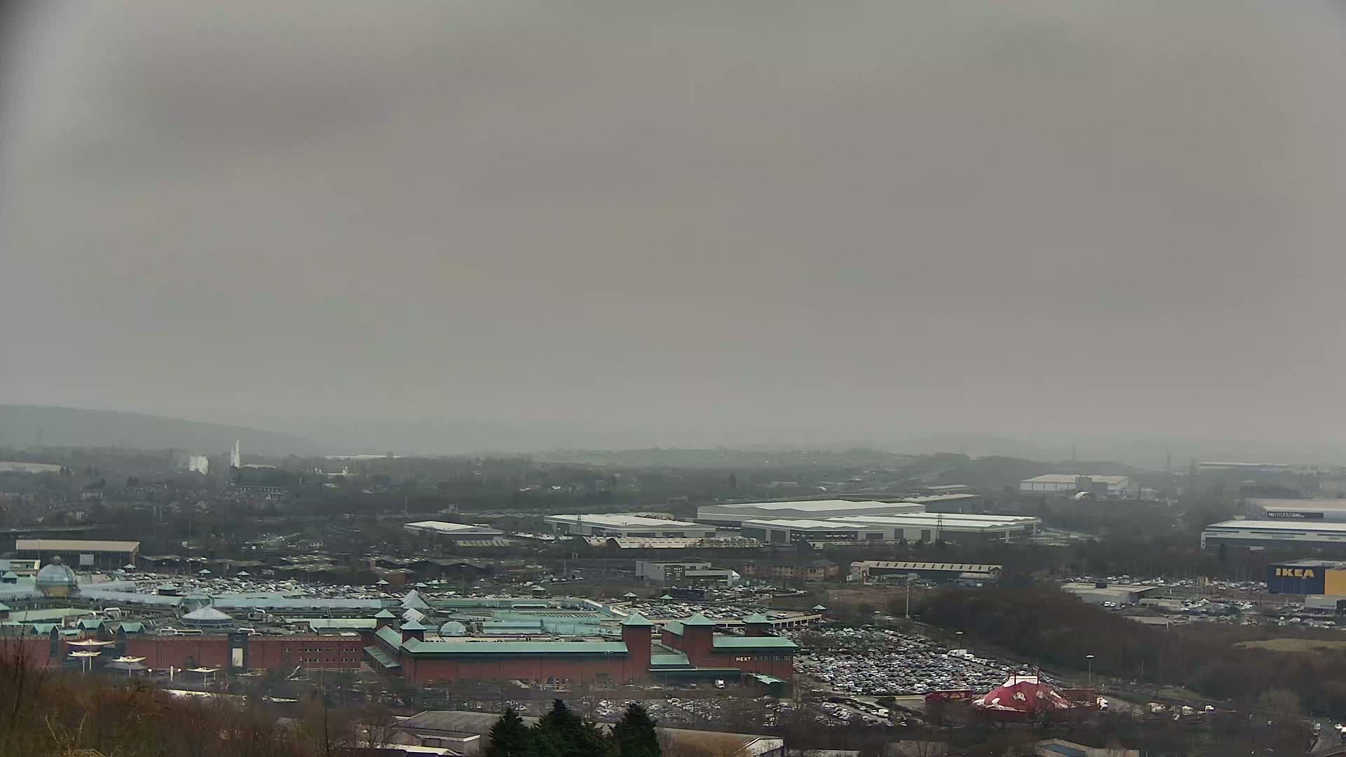 A sprawling shopping center and industrial area are visible under an overcast sky.