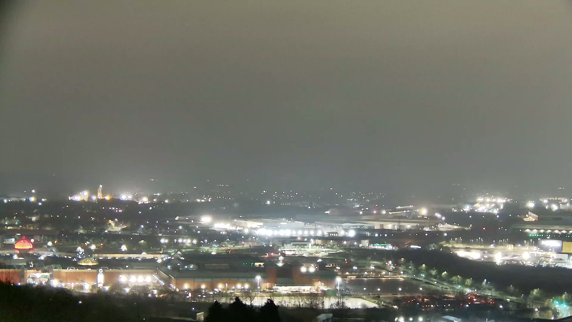 A hazy night view shows a sprawling cityscape illuminated by numerous lights, observed from a slightly elevated vantage point.