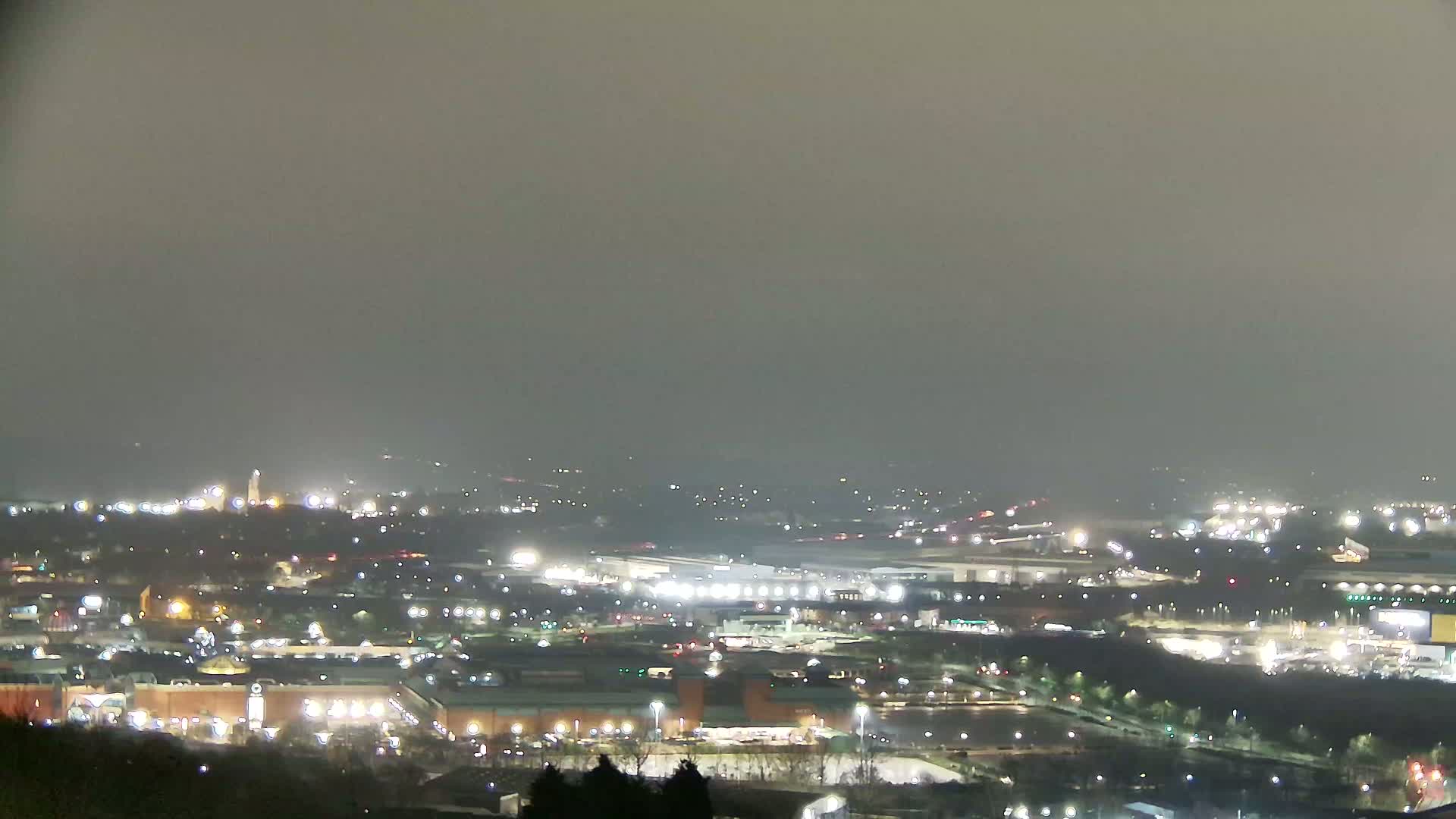 A nighttime view of a hazy city with numerous illuminated buildings and roads stretches into the distance.