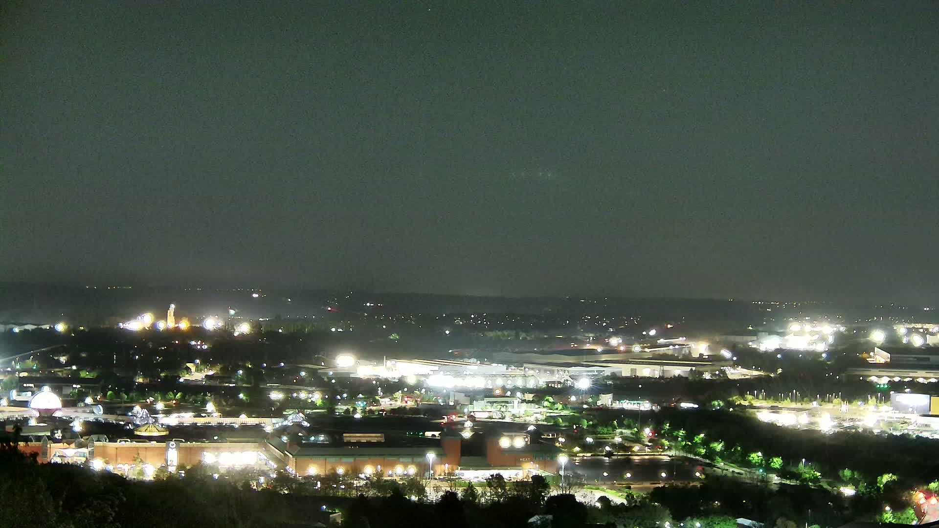 A nighttime, high-angle view of a sprawling city illuminated by artificial lights under a dark, overcast sky.