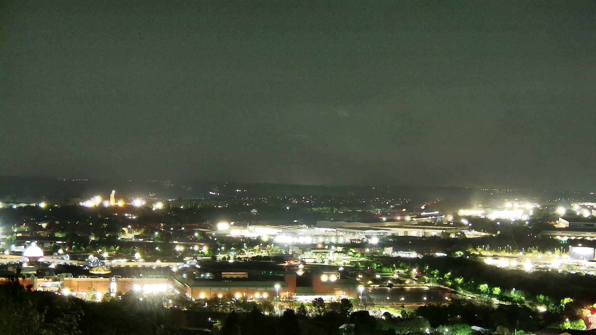 A nighttime, high-angle view of a sprawling city landscape illuminated by numerous lights under a dark, overcast sky.