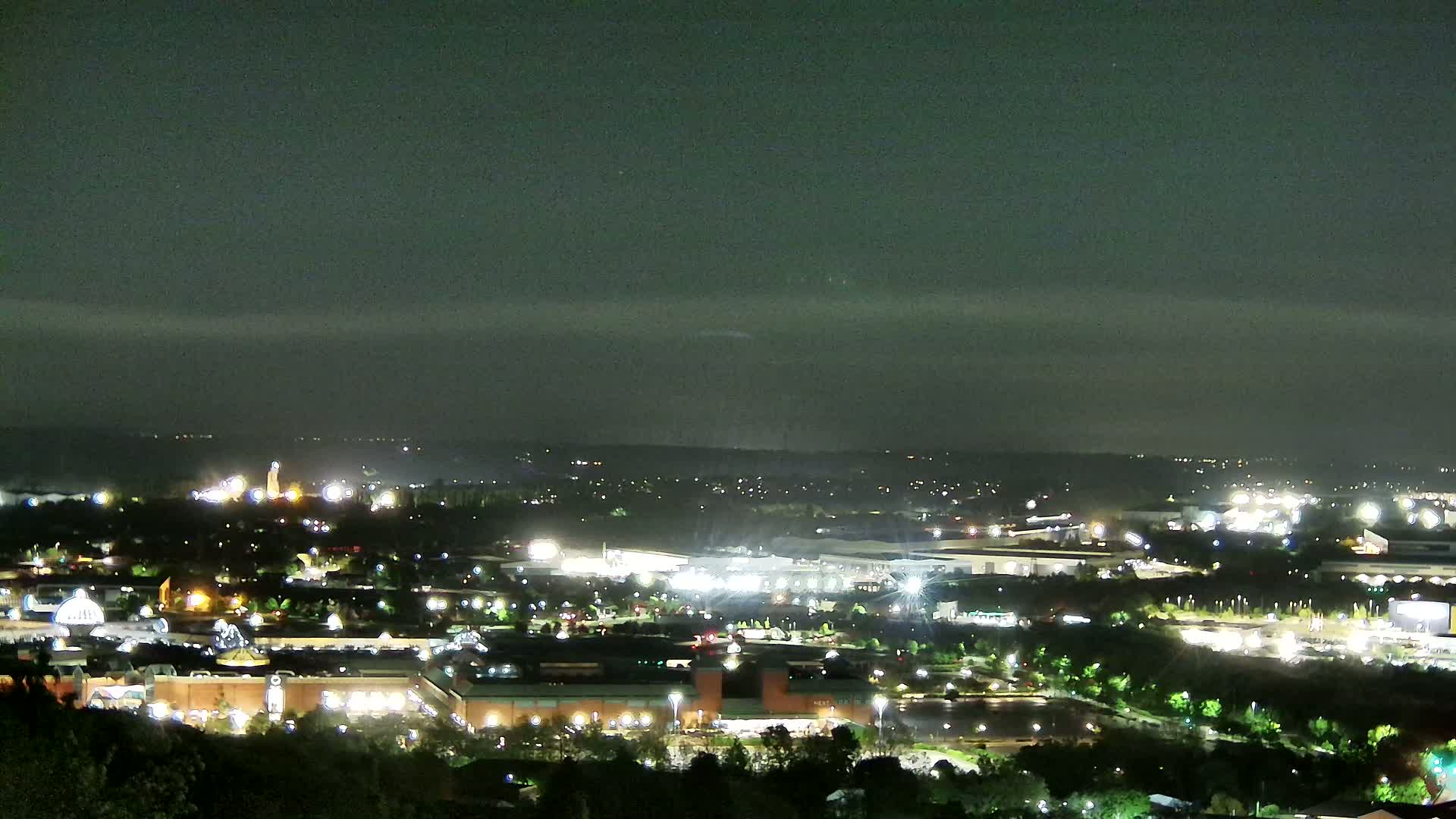 A nighttime view of a city illuminated by streetlights and building lights under a mostly cloudy sky.