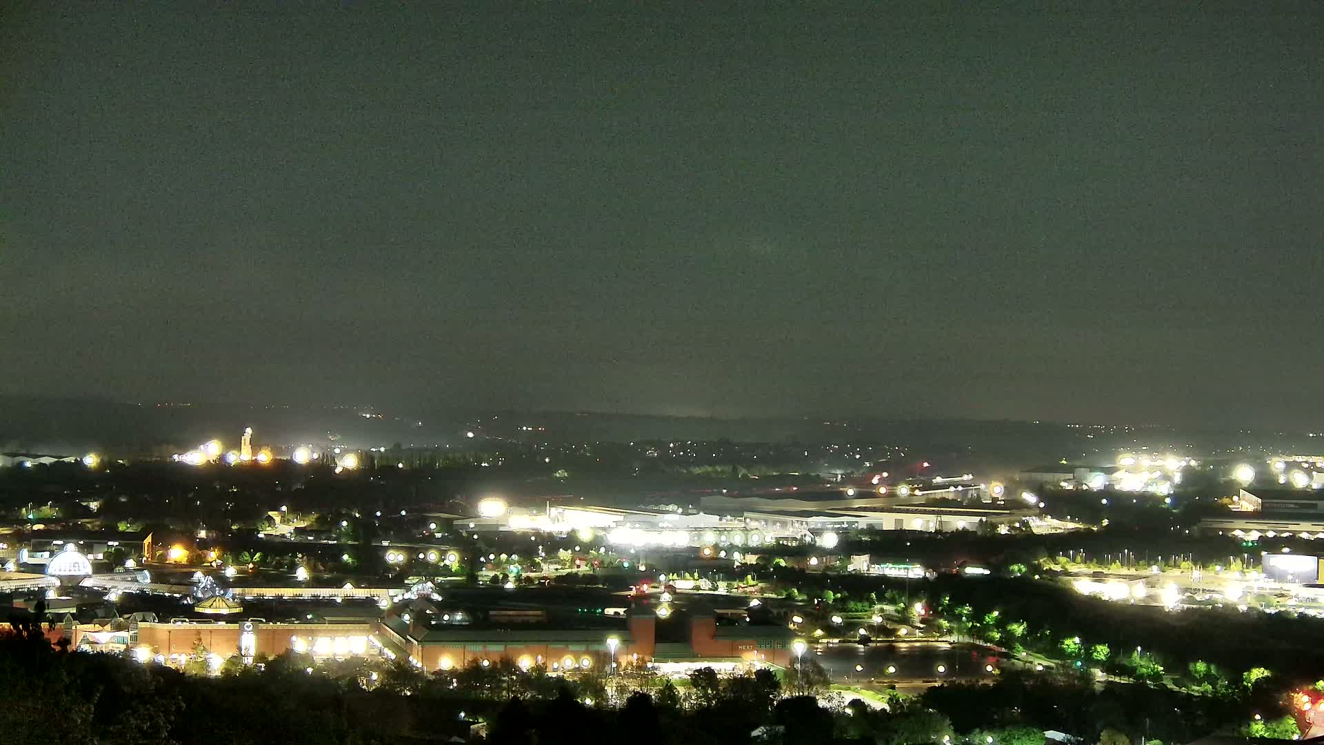 A nighttime, aerial view of a sprawling city illuminated by numerous lights under a dark, overcast sky.