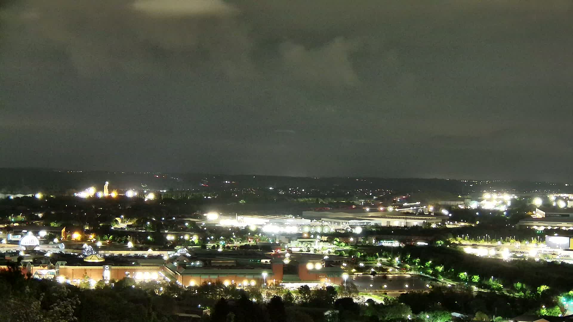 A nighttime view of a city illuminated by many lights under a cloudy sky.