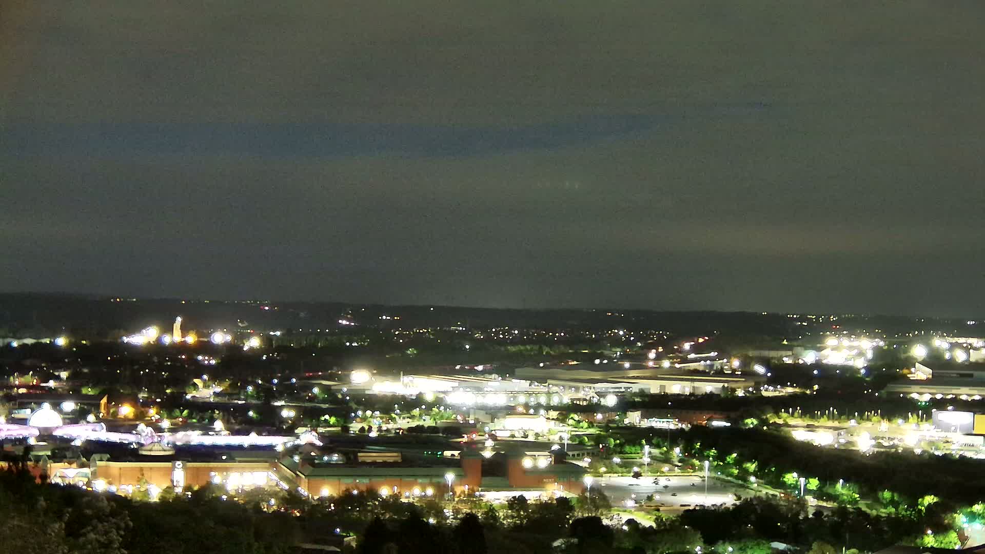 A nighttime view of a sprawling city illuminated by numerous lights under a dark, cloudy sky.