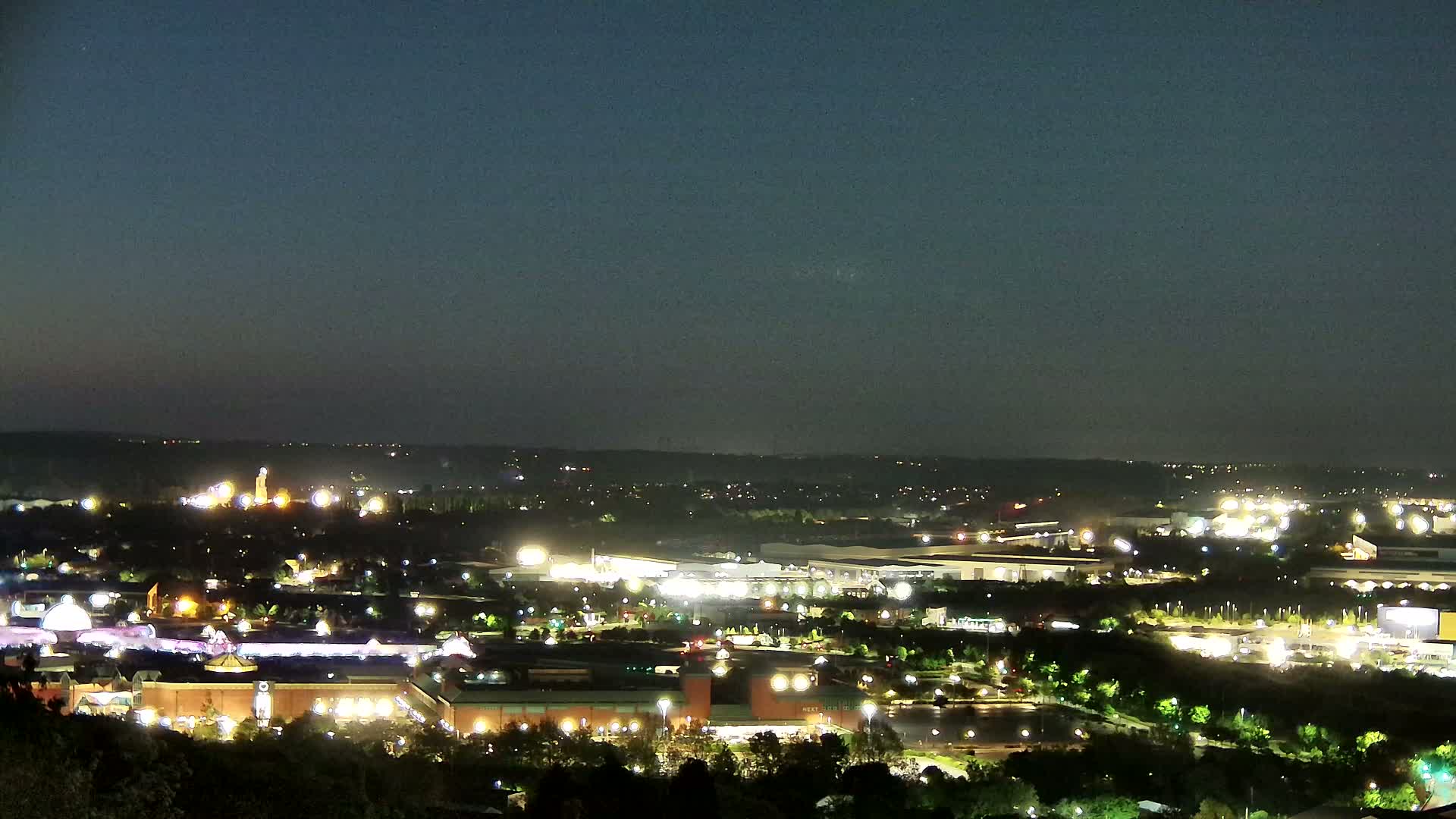 A nighttime view of a sprawling city landscape illuminated by numerous lights, under a clear, dark sky.