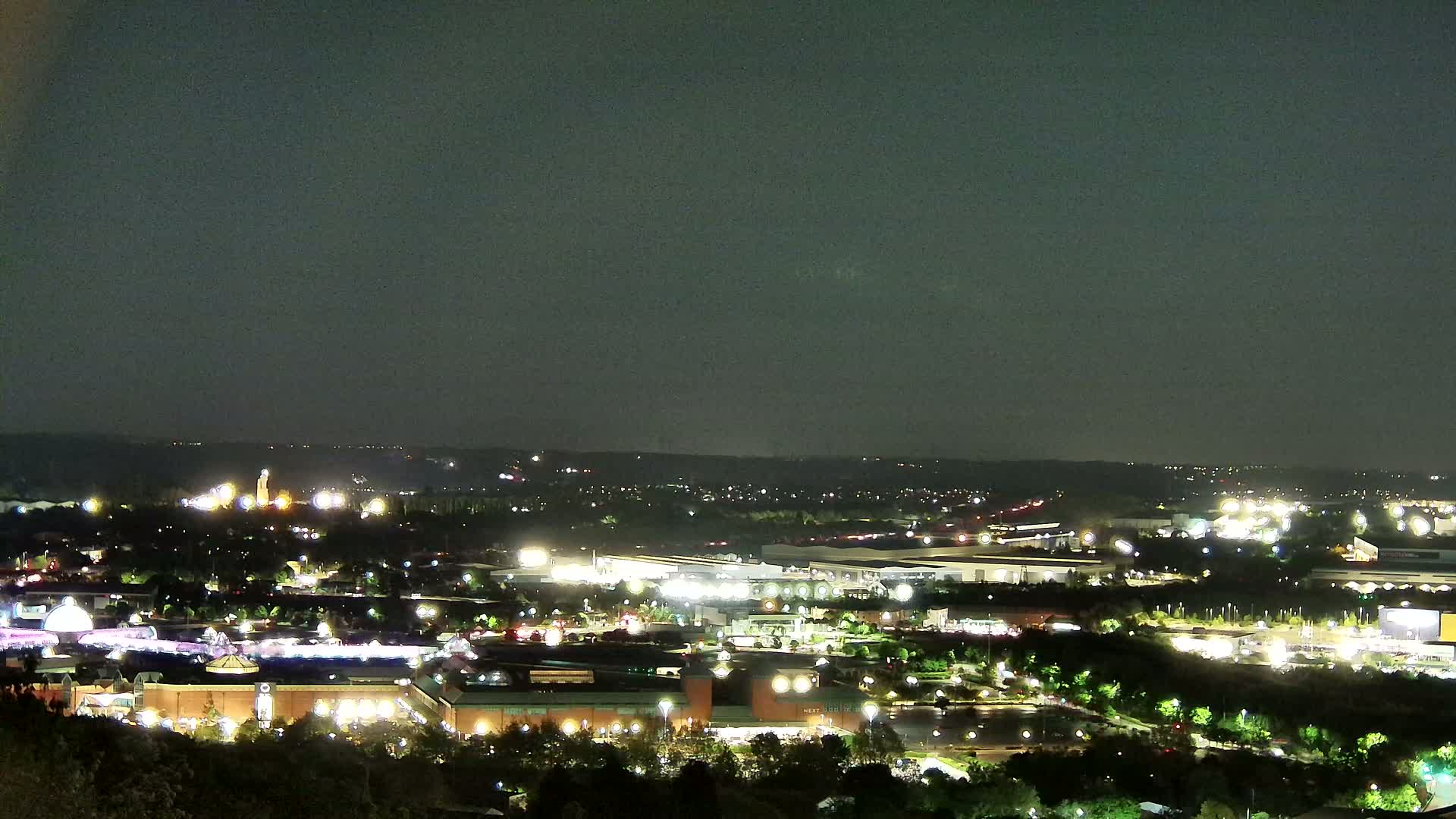 A nighttime, high-angle view of a city landscape illuminated by numerous lights, under a dark sky.