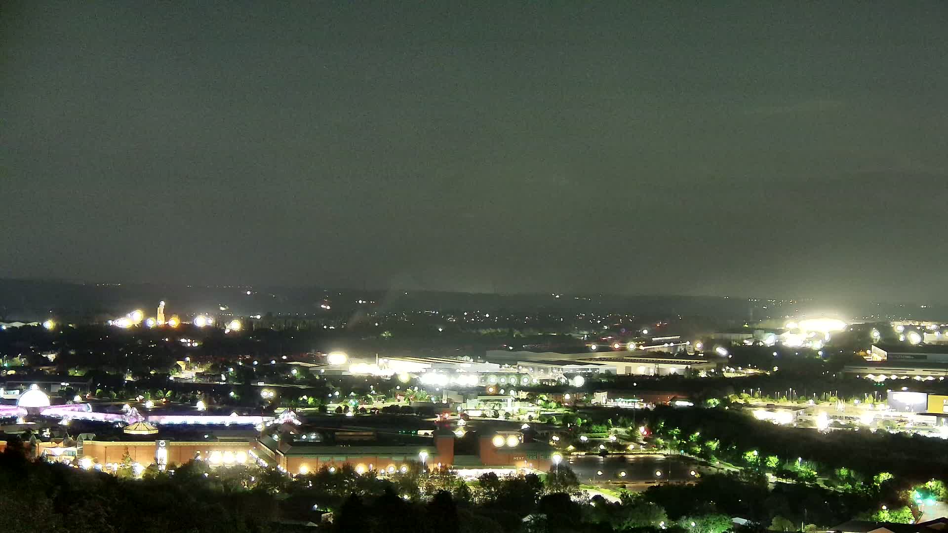 A nighttime, long-distance view of a city with numerous illuminated buildings and roads, under a dark, overcast sky.