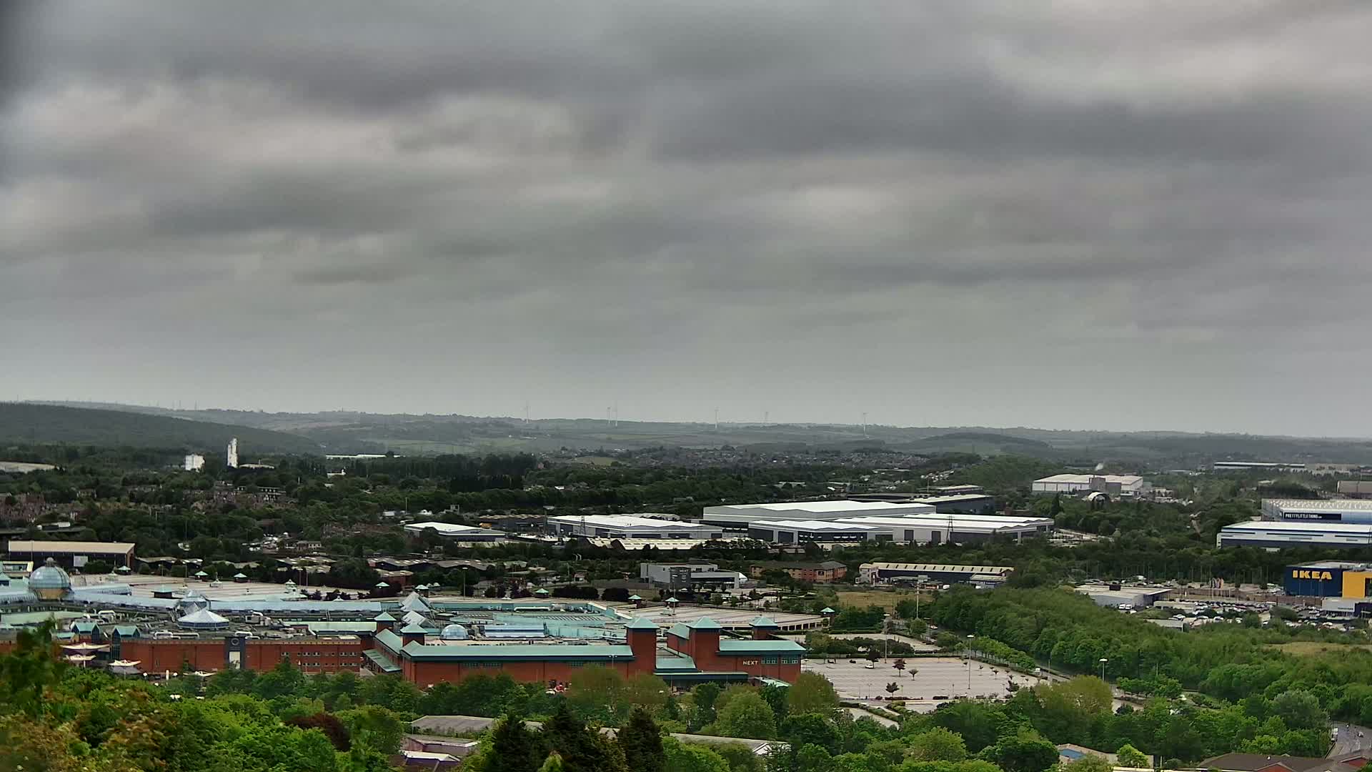 A sprawling shopping center and industrial park are visible beneath a cloudy sky.