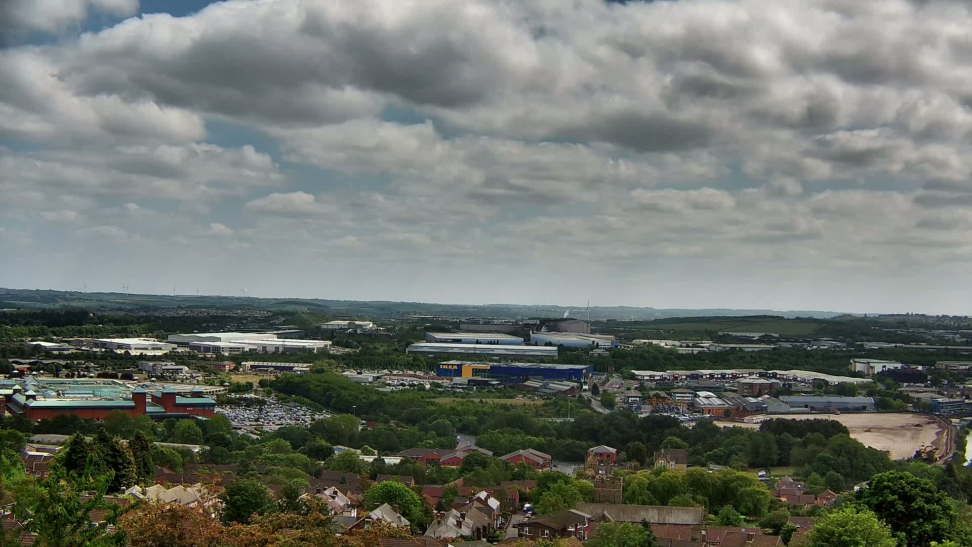 A high-angle view of a suburban area with industrial buildings and a large parking lot under a partly cloudy sky.