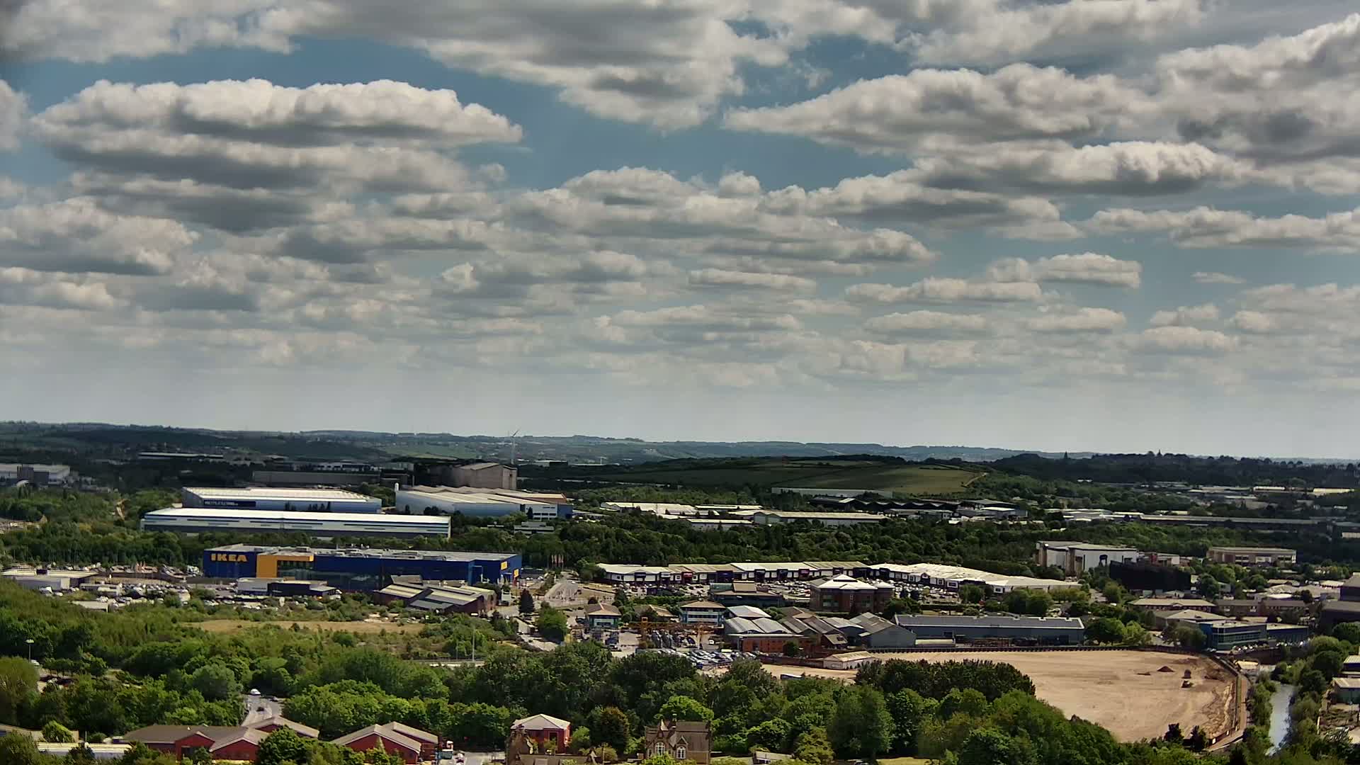 An aerial view shows a sprawling industrial park and retail area under a partly cloudy sky.