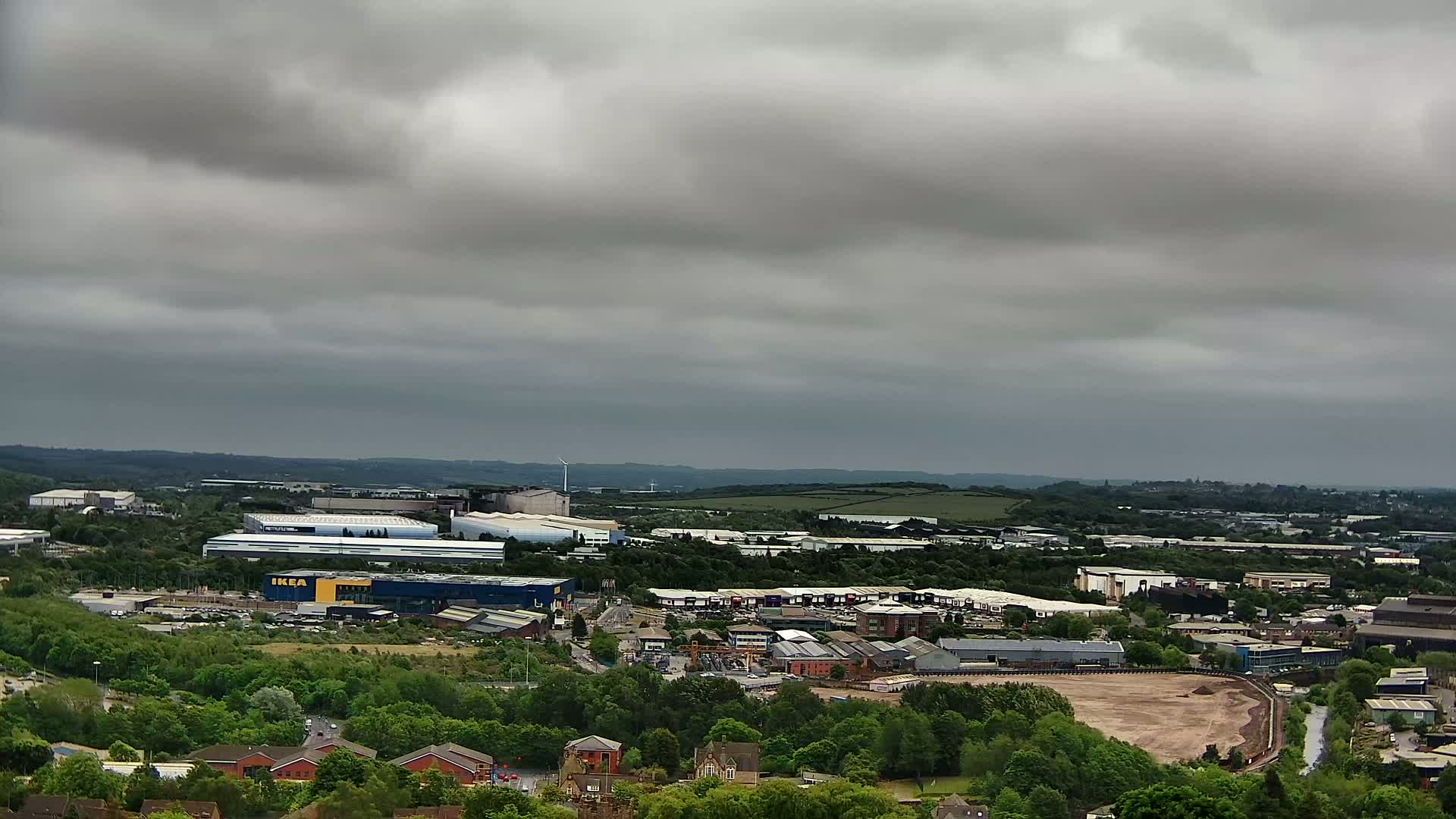 A sprawling industrial area with an IKEA store, surrounded by green trees and under a cloudy sky.