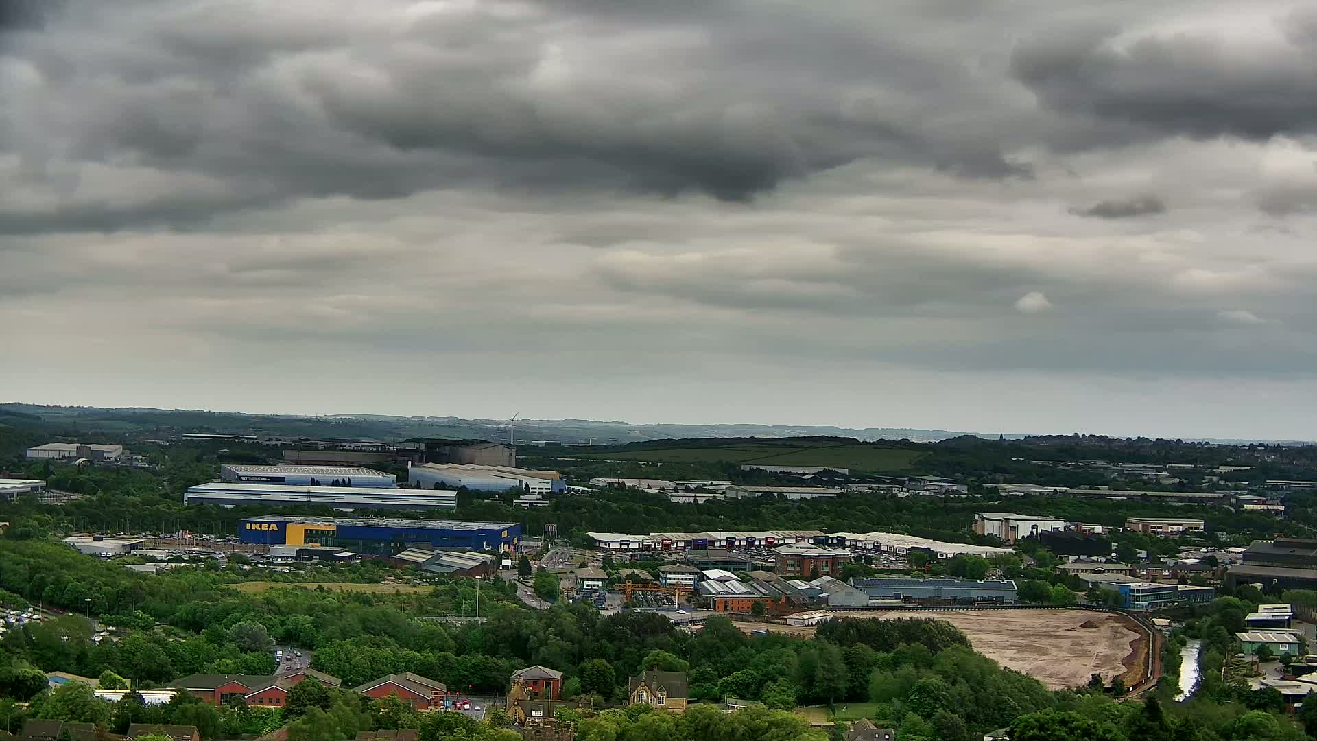 An expansive view of an industrial area and surrounding green landscape under a cloudy sky.