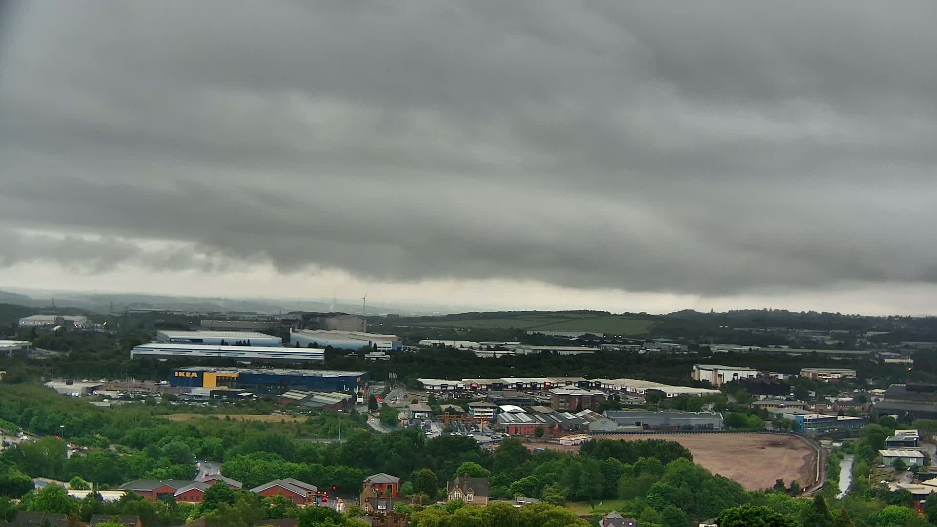 An aerial view of an industrial area and surrounding green spaces under a heavily overcast sky.