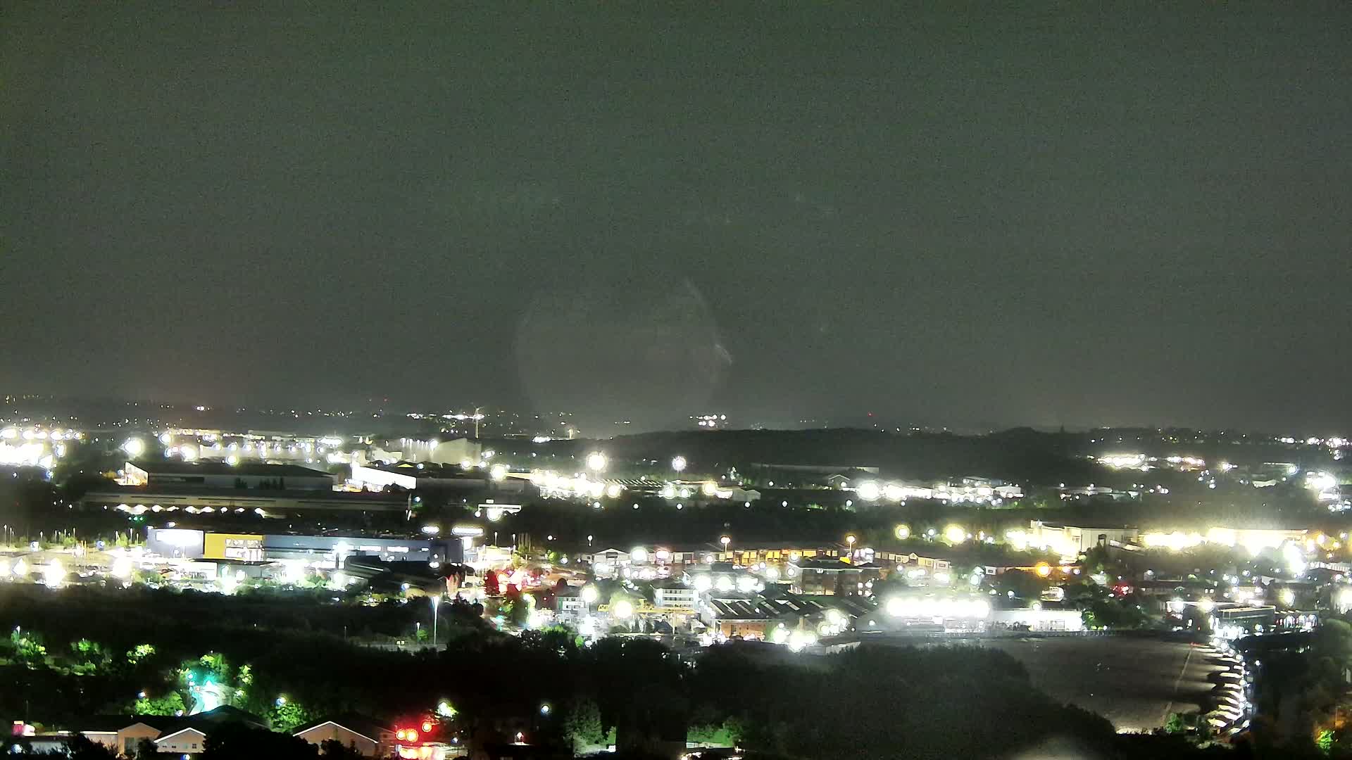 A nighttime view of a suburban area with many lit buildings and roads under a dark, cloudy sky.