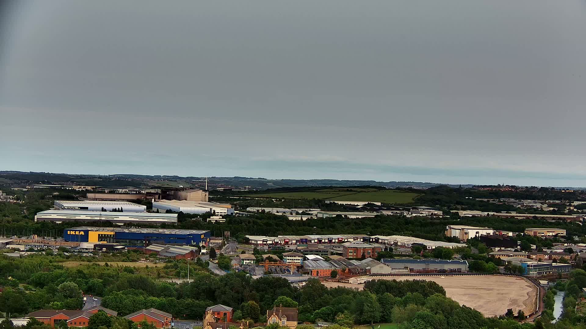An aerial view shows an industrial area with an IKEA store, surrounded by buildings and green spaces, under an overcast sky.