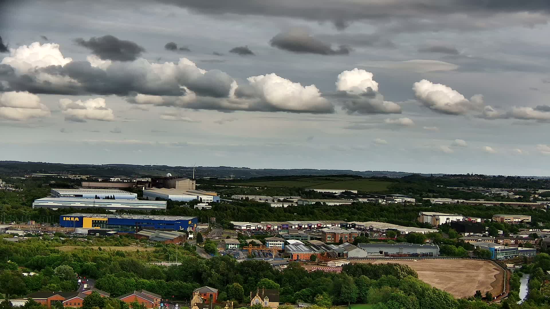 An aerial view of an industrial area with several buildings, including a large blue and yellow building, under a partly cloudy sky.