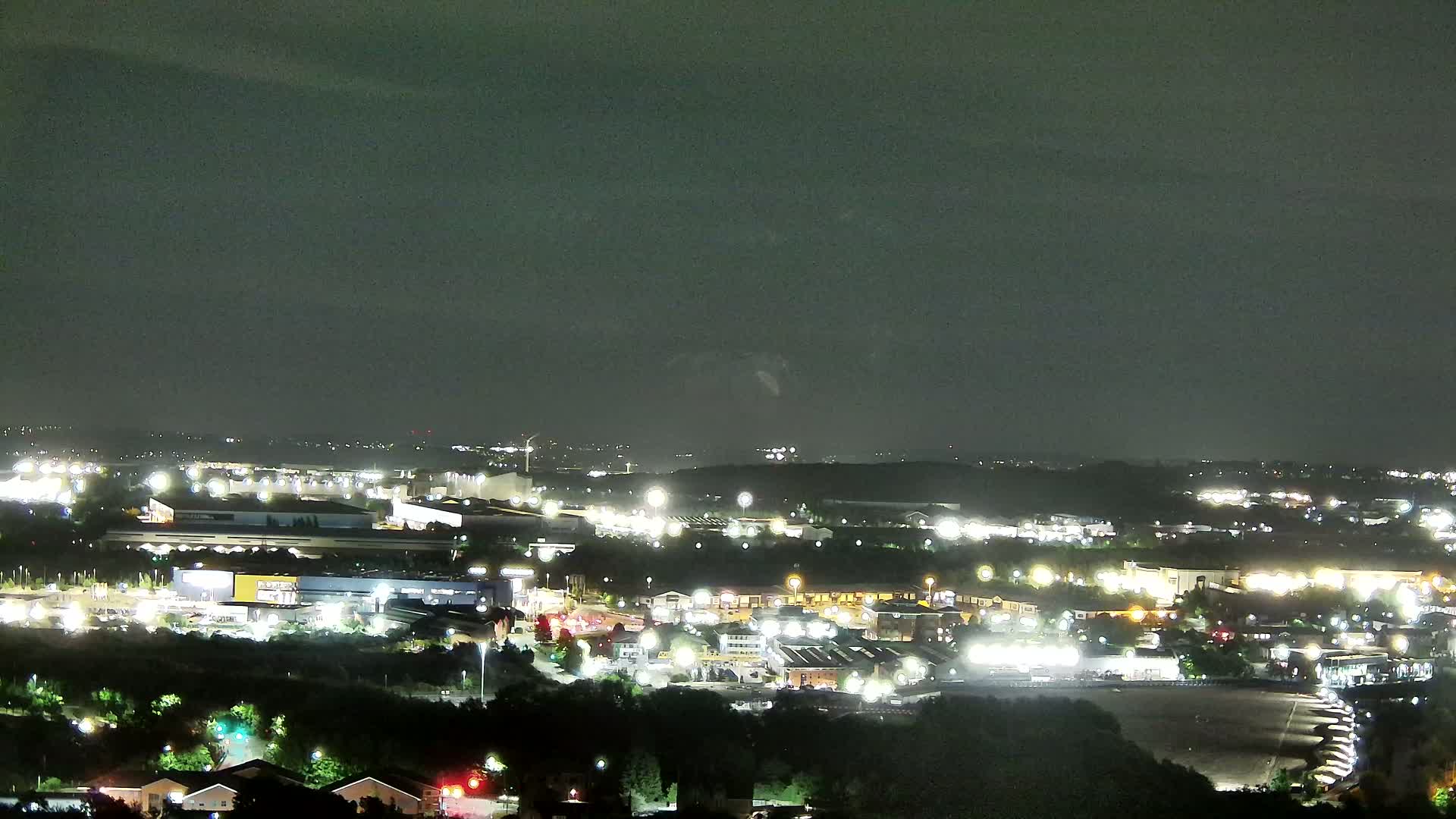 A nighttime, high-angle view of a sprawling illuminated industrial and commercial area, with a dark sky overhead.