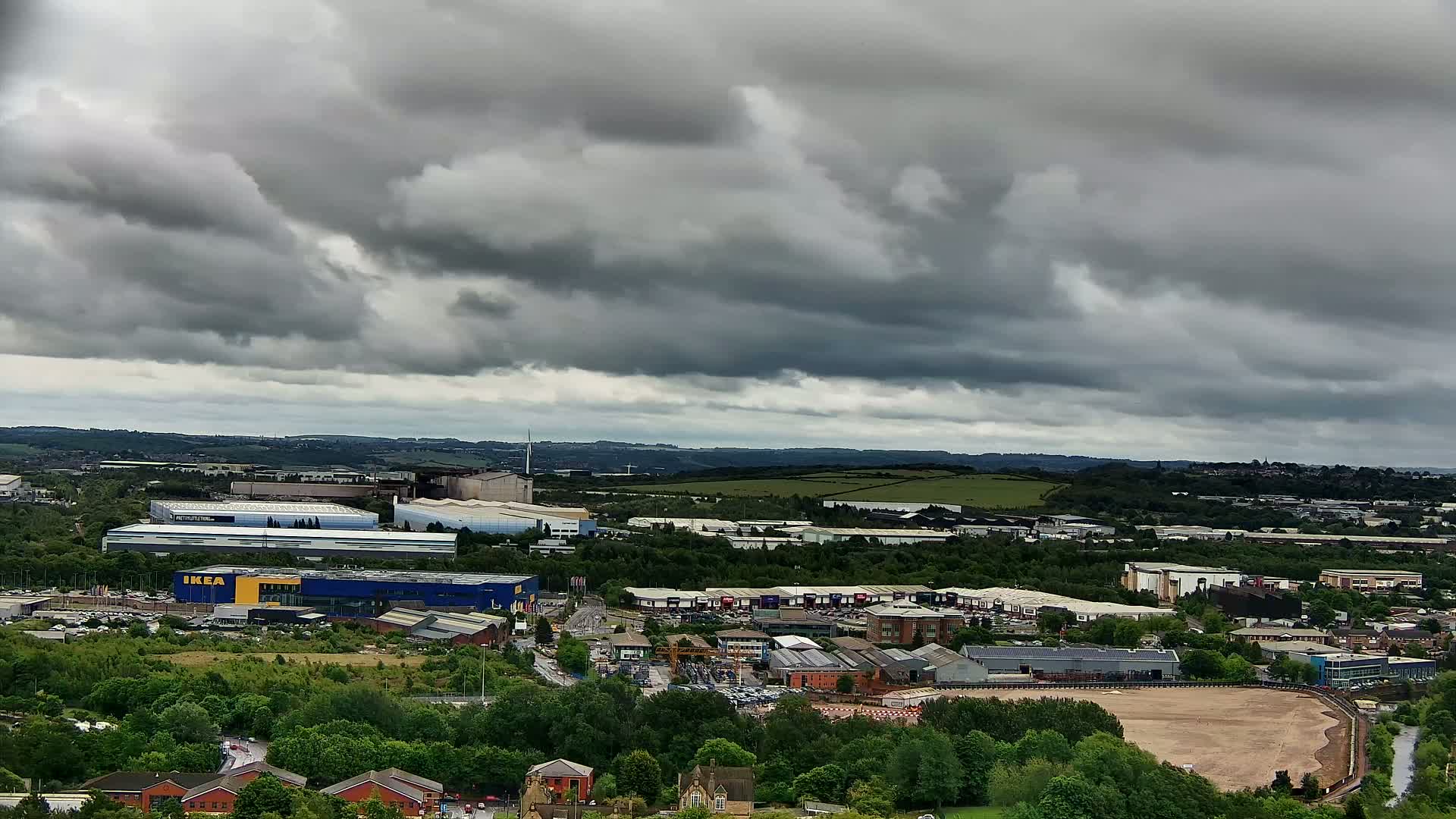 An aerial view of an industrial area with numerous buildings, surrounded by greenery, under a heavily clouded sky.