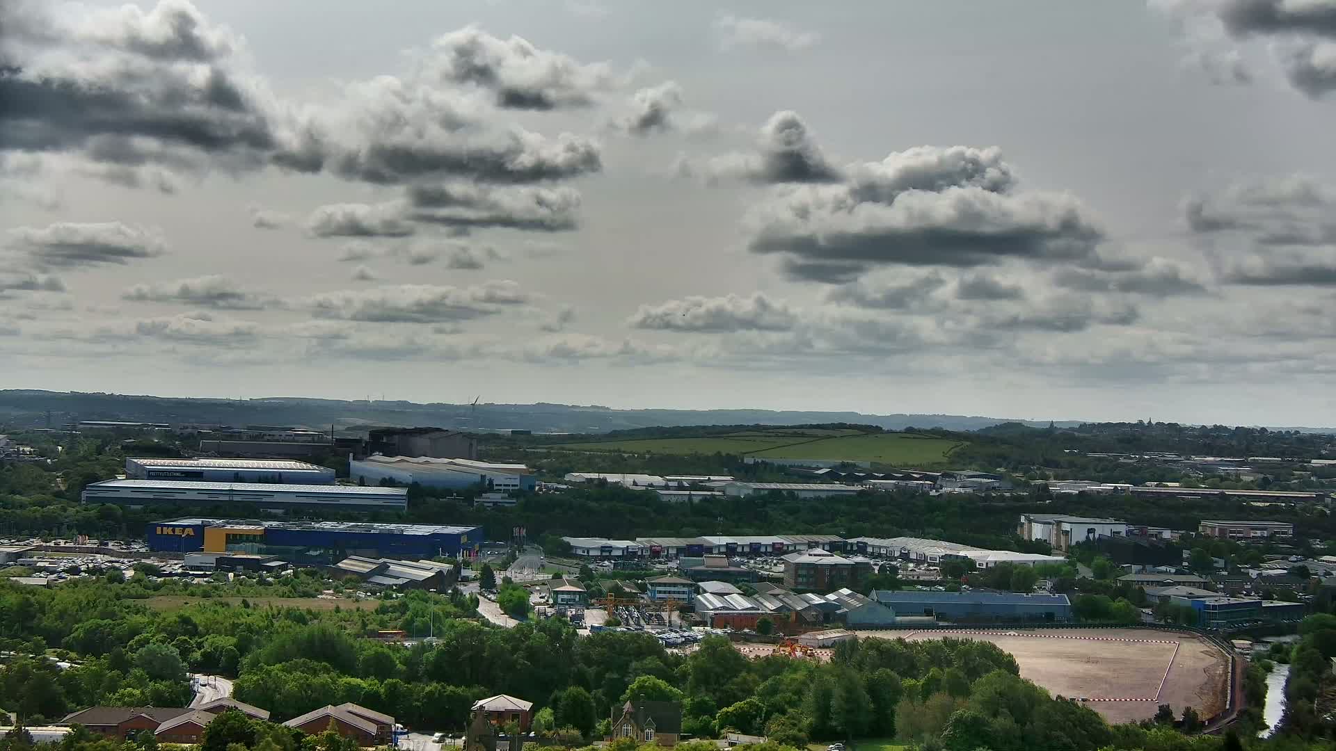 An expansive view of a landscape dotted with industrial buildings and greenery under a partly cloudy sky.