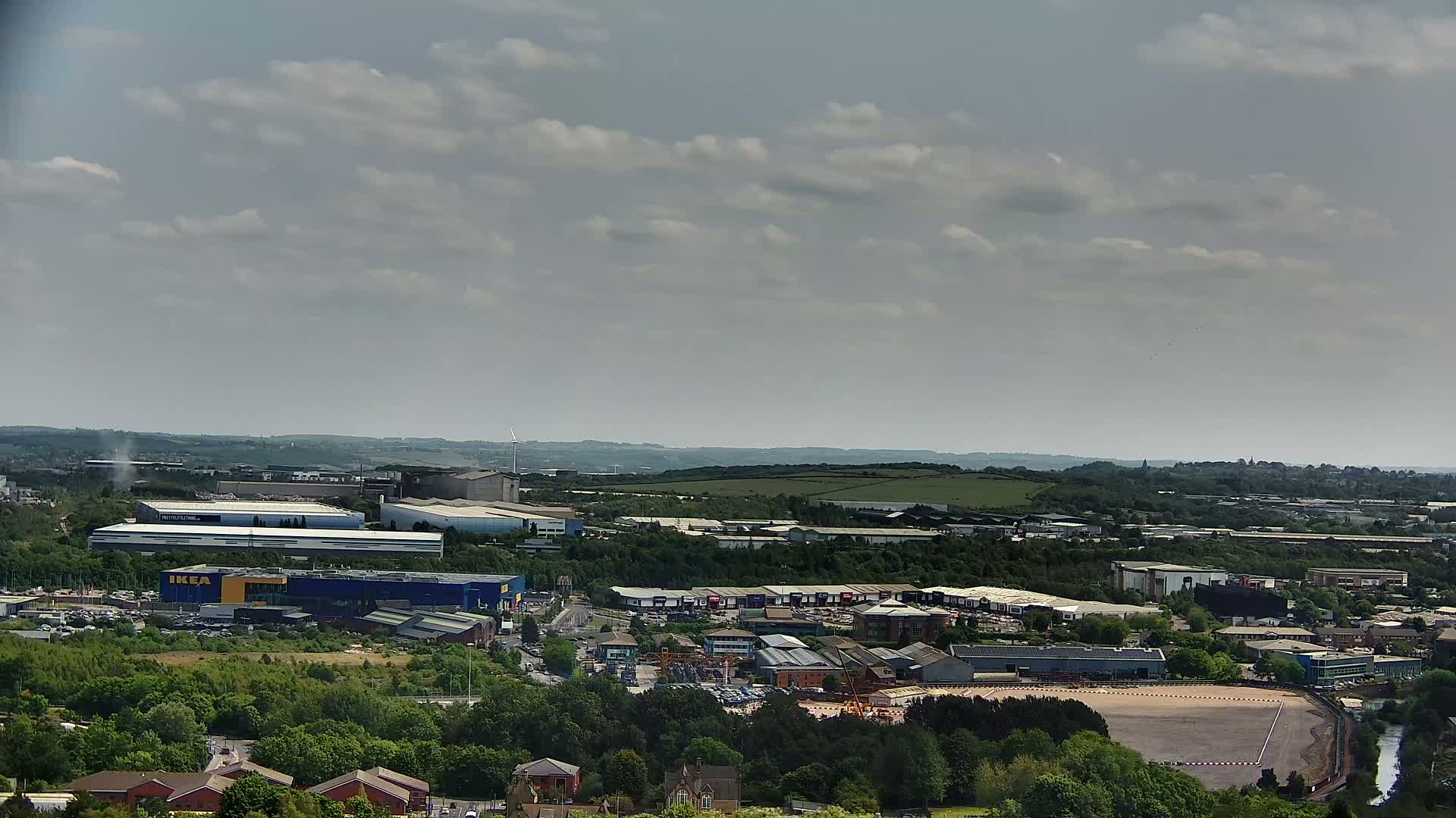 A sprawling industrial area with a large blue-and-yellow building, surrounded by greenery and under a partly cloudy sky.