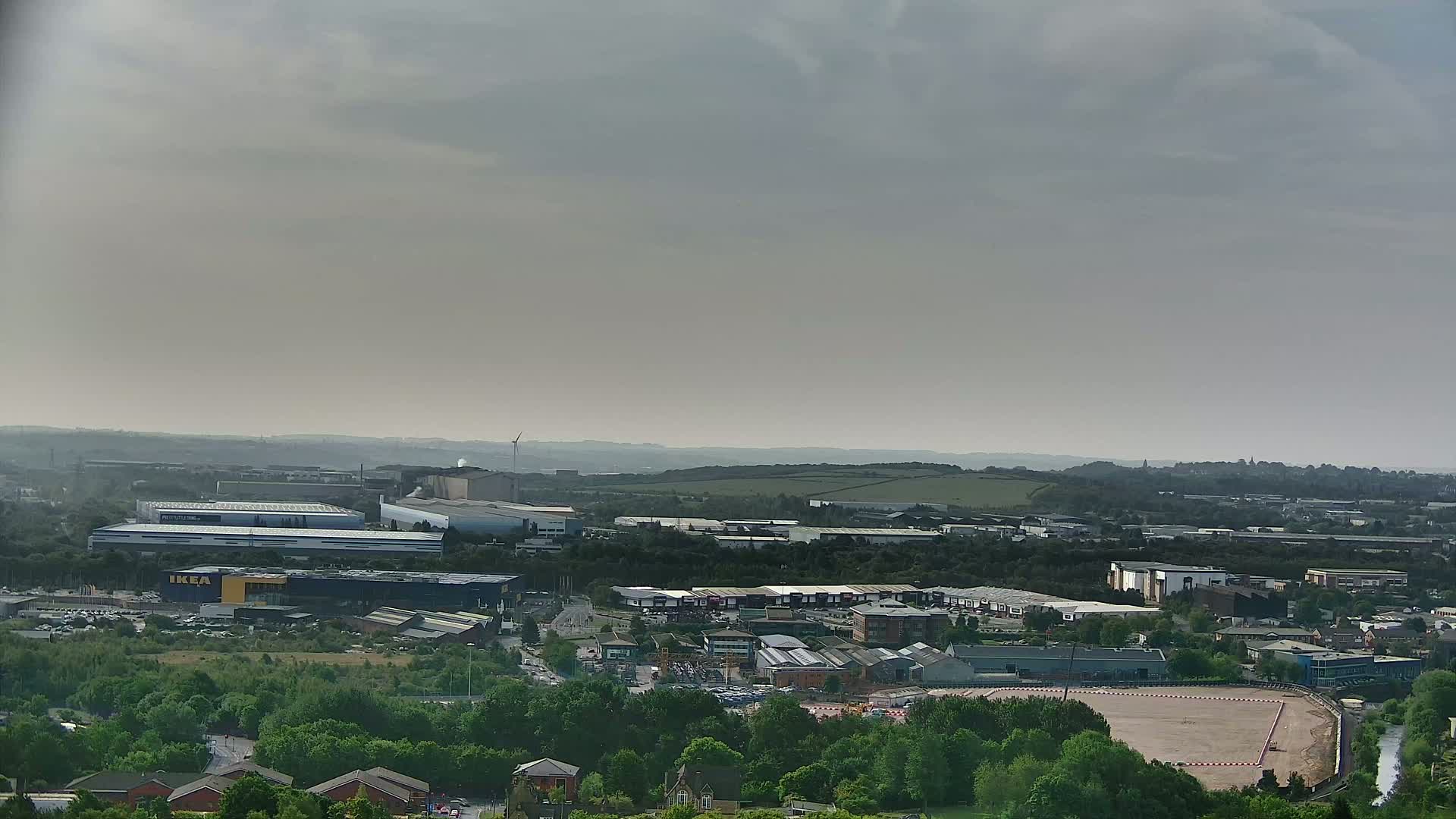A sprawling industrial and commercial area, dotted with buildings and greenery, stretches under a hazy sky.