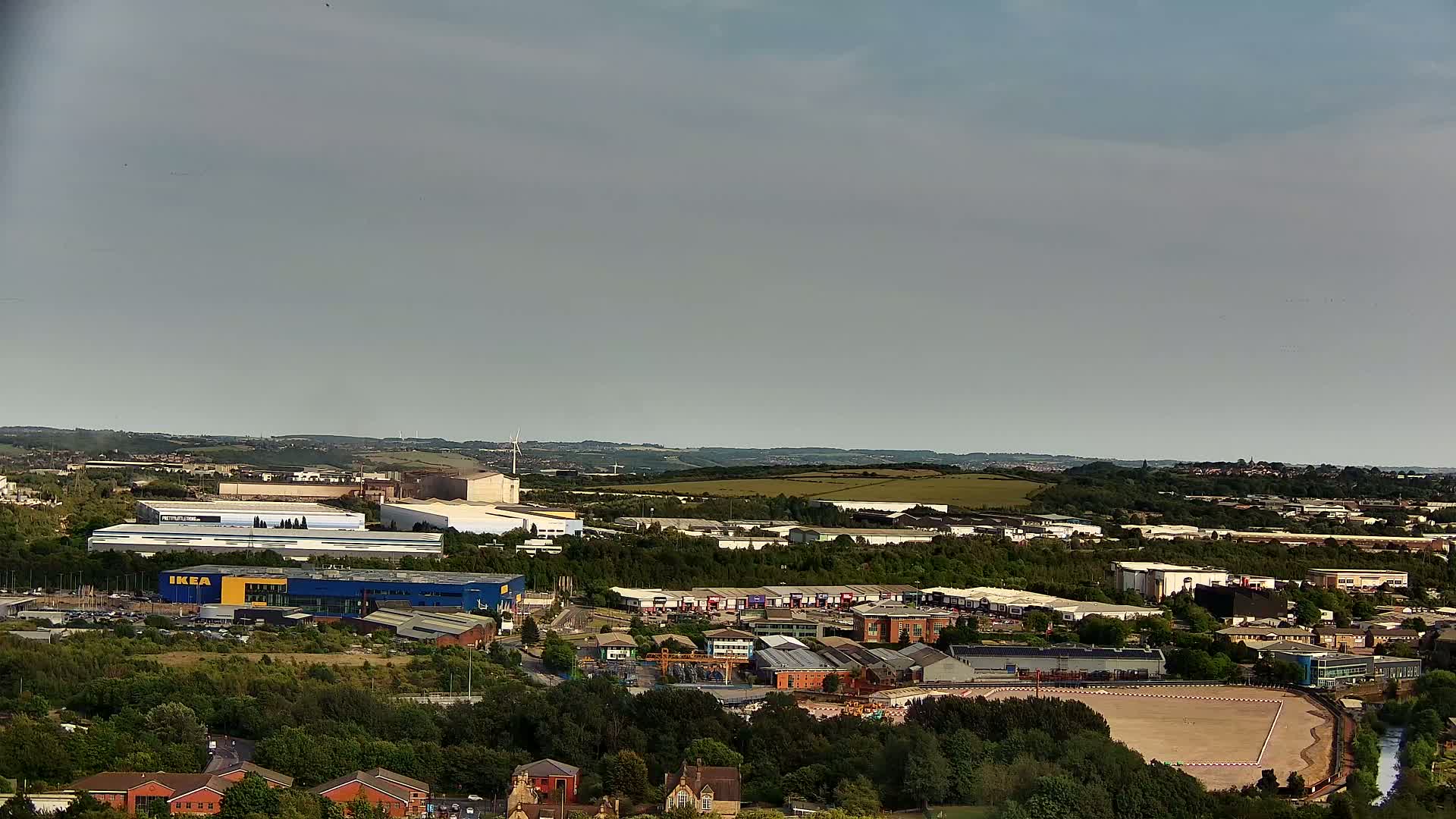 An expansive view of an industrial area, featuring a large blue building and numerous other structures, under a mostly cloudy sky.