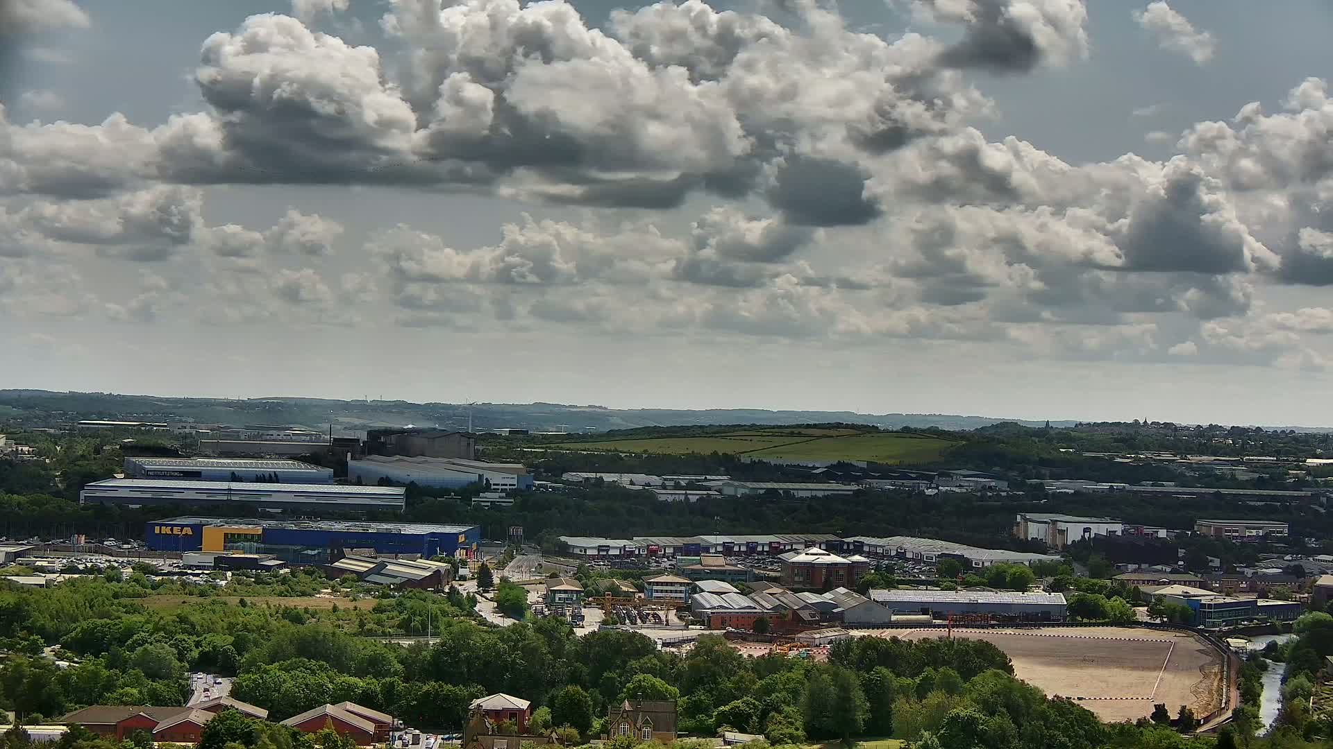 A high-angle view of an industrial area with numerous buildings and a large parking lot under a partly cloudy sky.