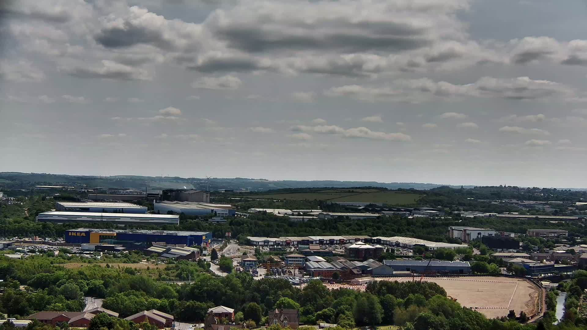 An expansive view of an industrial area with an IKEA store, surrounded by greenery and under a partly cloudy sky.