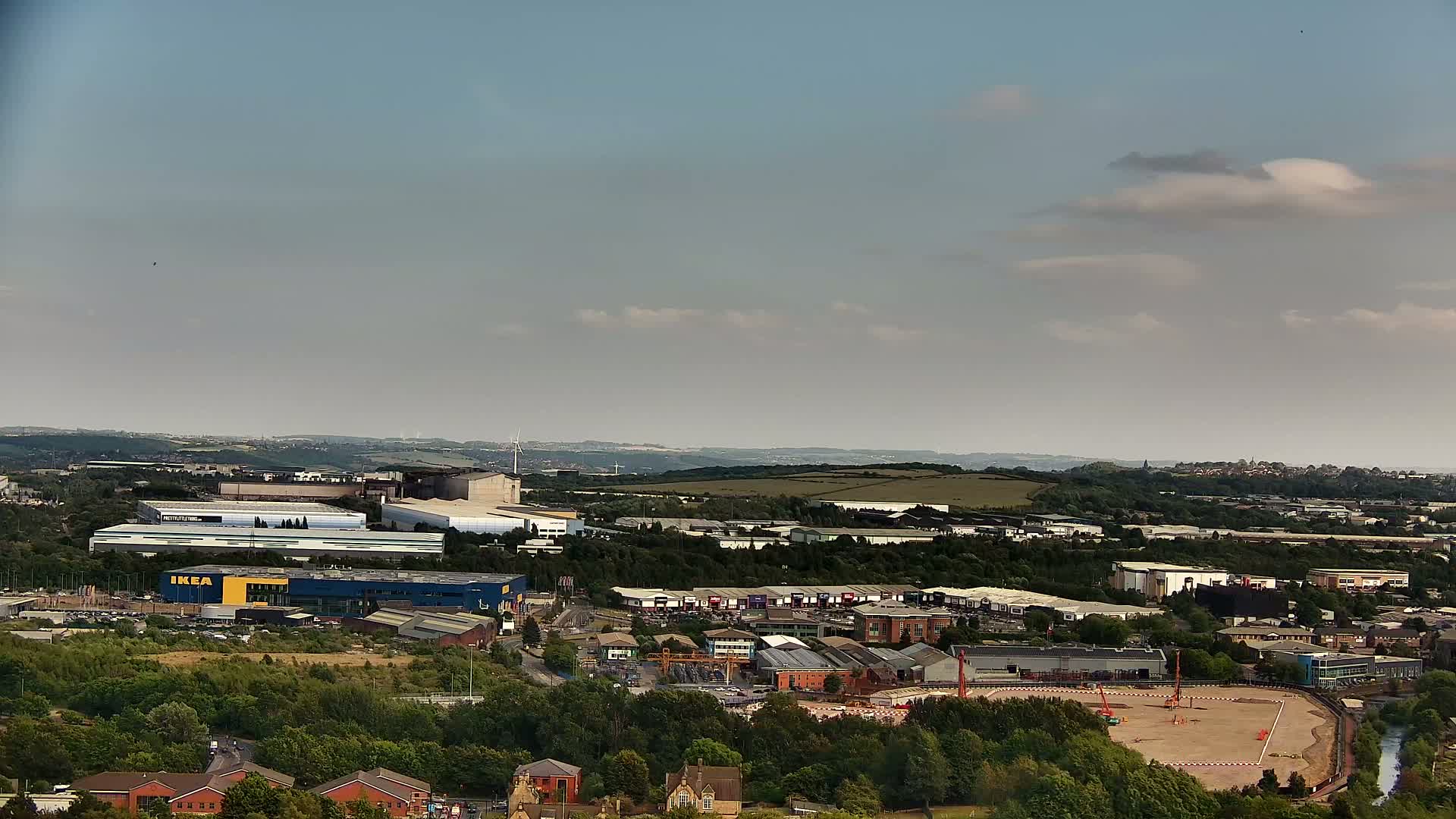 A high-angle, long shot shows a sprawling industrial area with an IKEA store, surrounded by other buildings and green spaces under a mostly clear, slightly hazy sky.