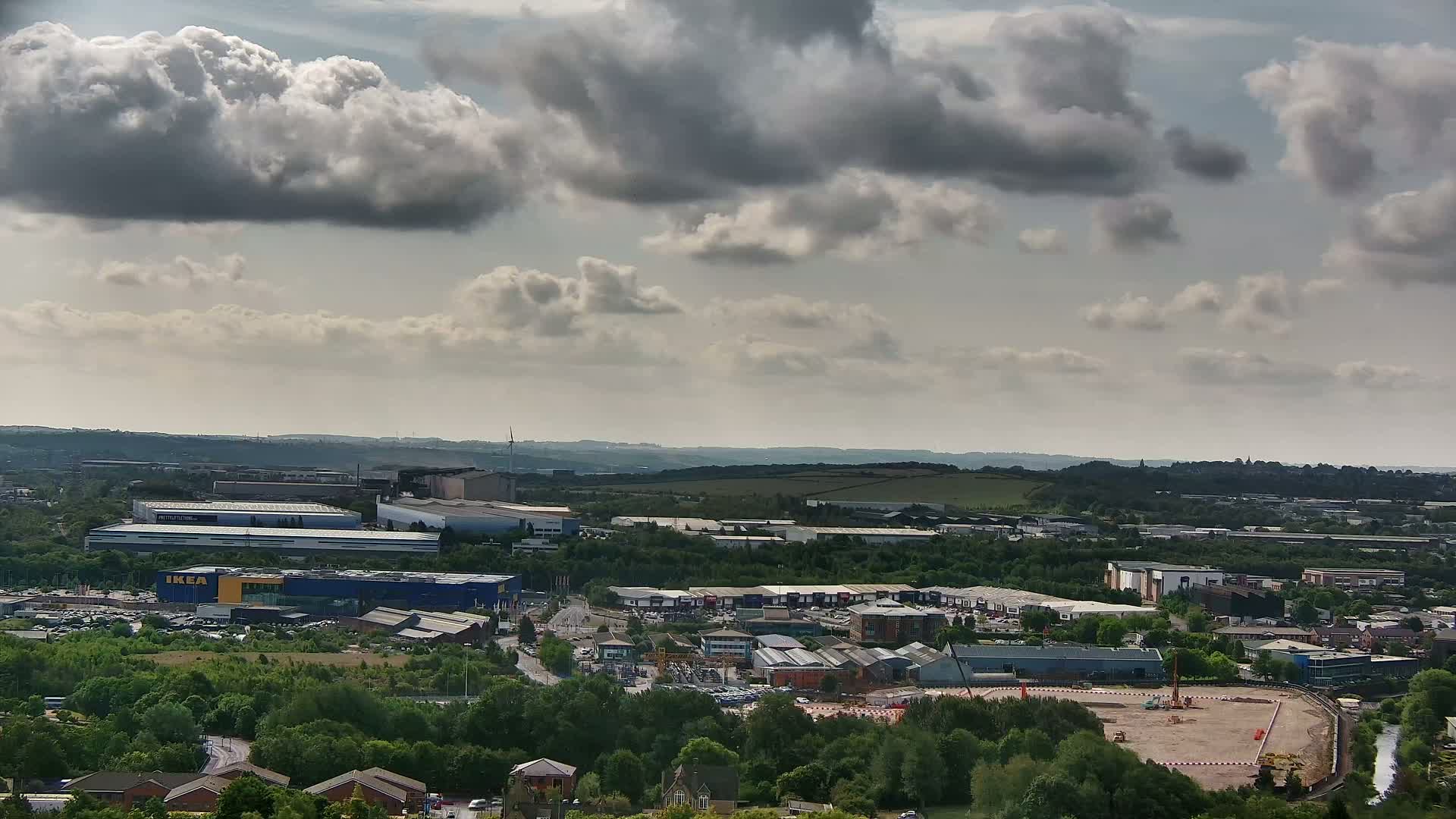 A high-angle, long shot of an industrial area with a large blue building, under a partly cloudy sky.