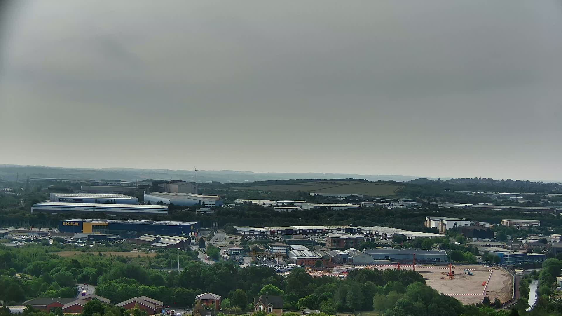 An aerial view shows an industrial and commercial area with numerous buildings, including a large blue building, under a hazy, overcast sky.