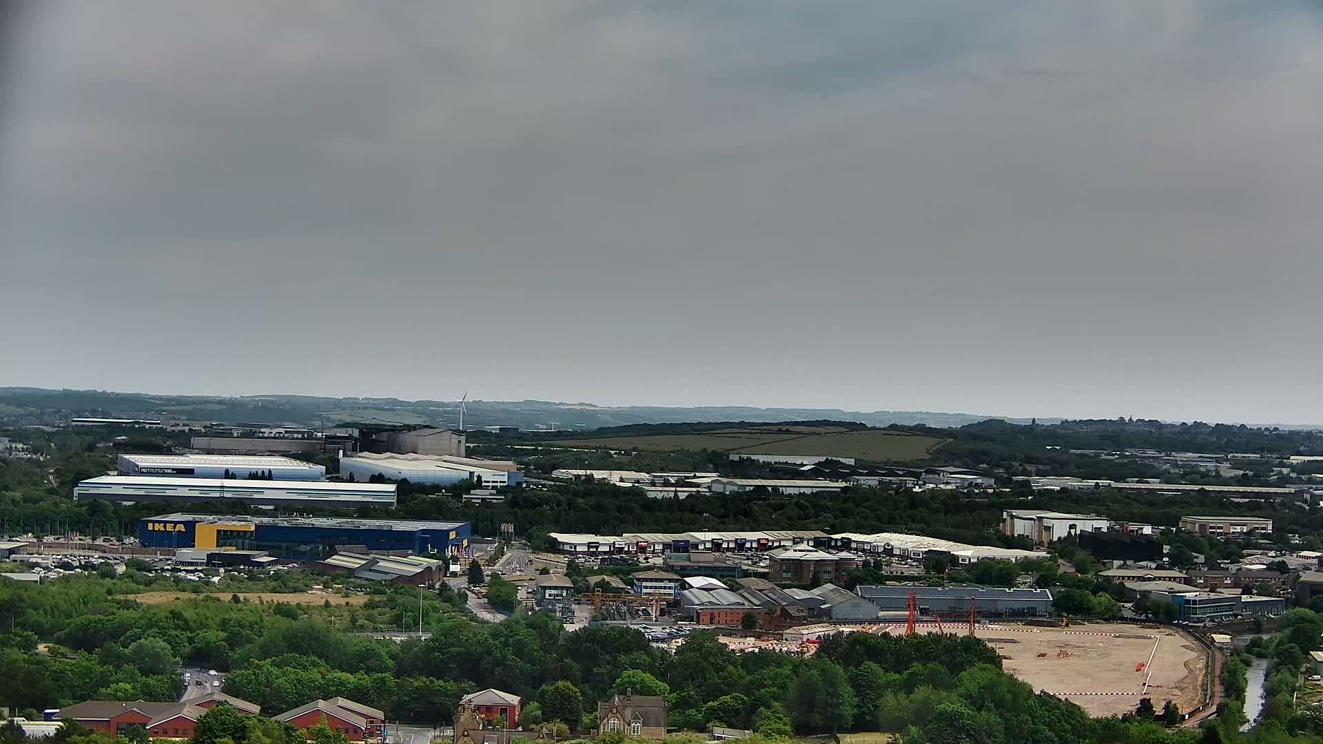 An expansive view of an industrial area with various buildings, including a large blue-roofed structure, under an overcast sky.
