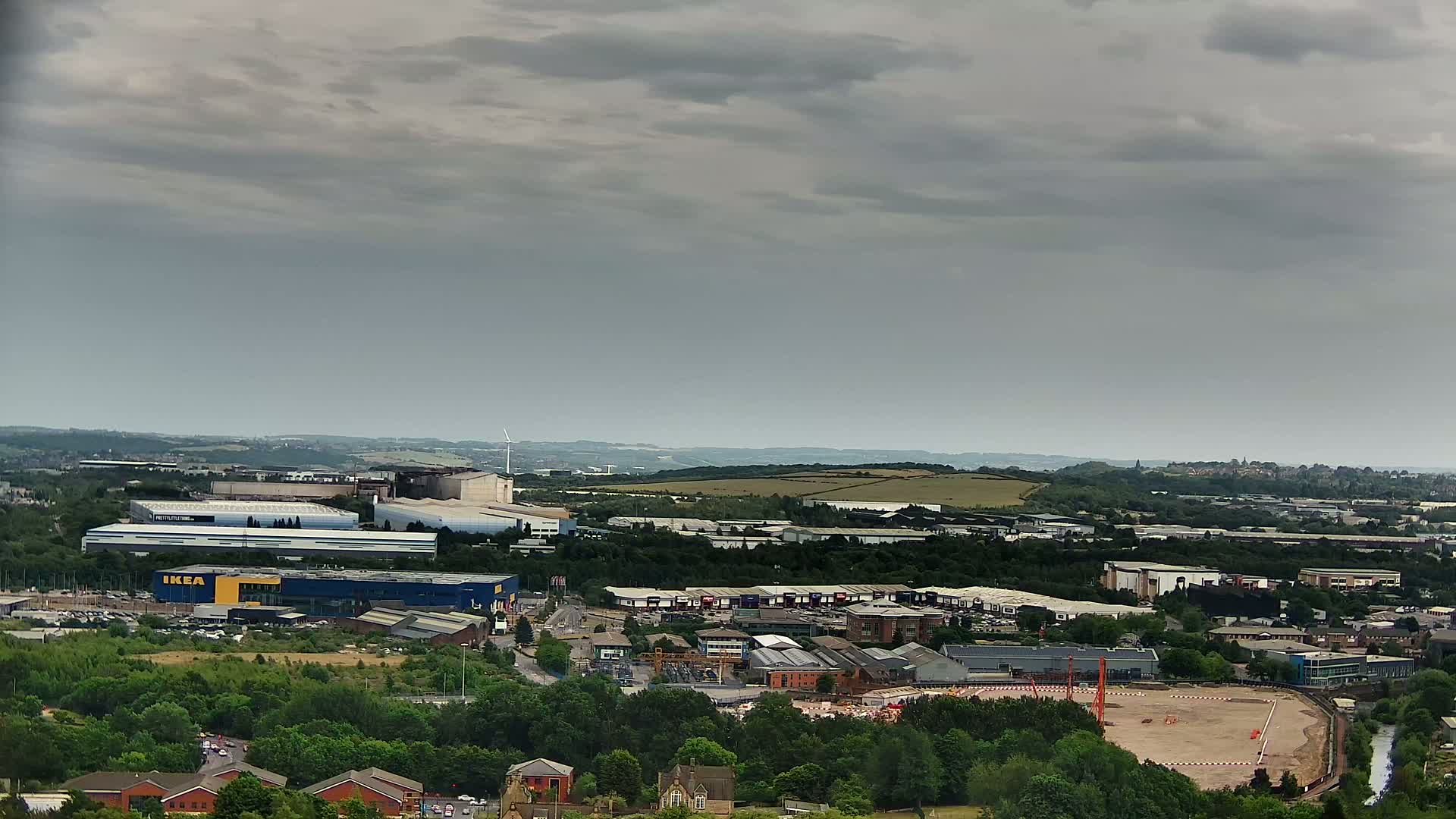 An expansive view of an industrial area, featuring various buildings and a large empty construction site, under a cloudy sky.